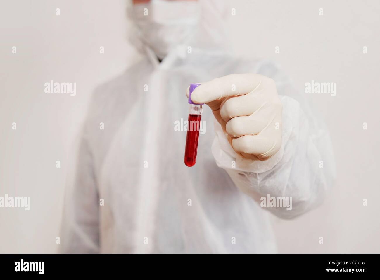 un tecnico di laboratorio in una tuta protettiva e maschera contiene una fiala piena di sangue per l'analisi di virus o malattie. Test del DNA. Mano che tiene un sangue Foto Stock