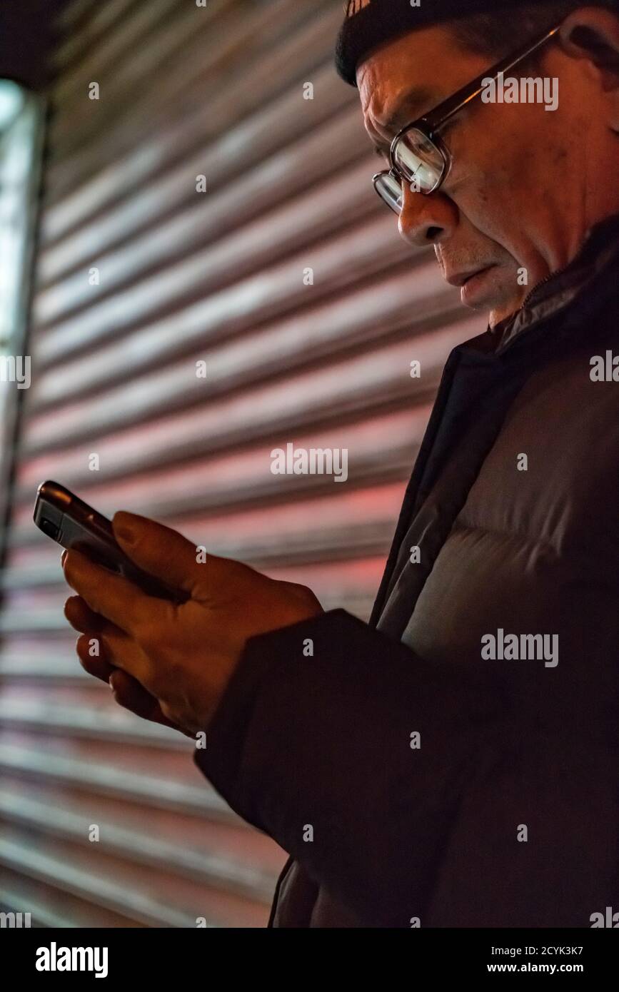 La città di New York New York, Feb 14, 2018: l'uomo guarda il suo smart phone davanti a un negozio griglia Foto Stock