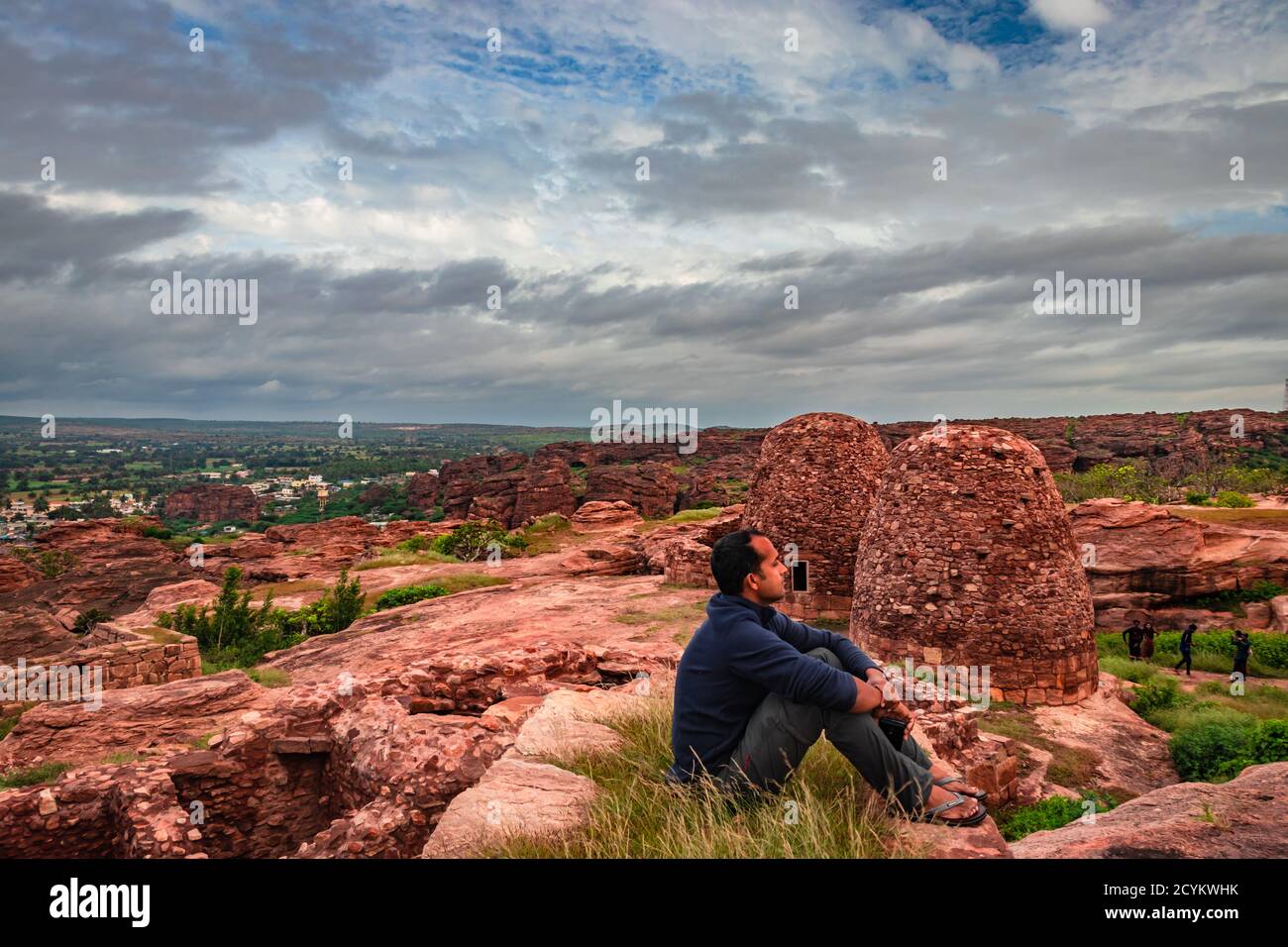 l'uomo seduto in cima alla montagna e guardando le rovine del forte storico al mattino viene scattata a badami karnataka india. Foto Stock
