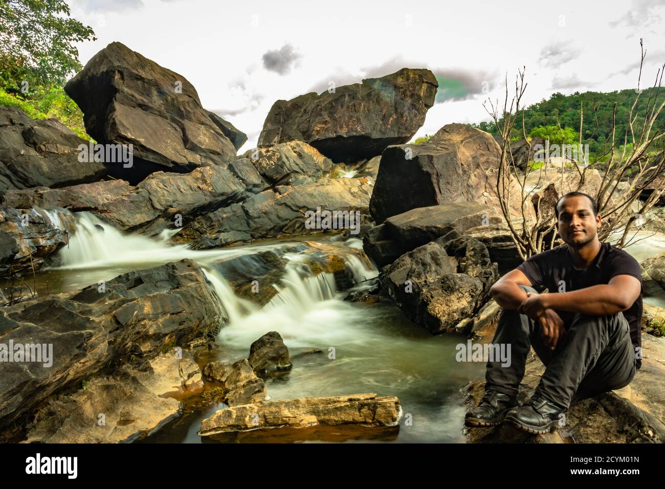 uomo seduto alla roccia guardando la bella cascata ruscello lungo l'esposizione scattata in serata viene ripresa in un punto occidentale remoto ghat foreste karnataka indi Foto Stock