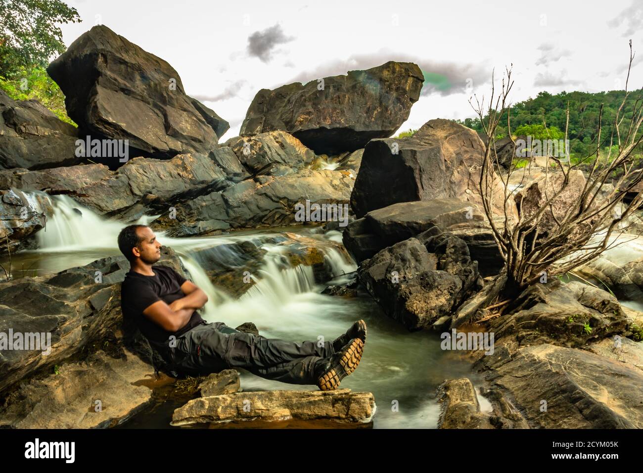l'uomo che si rilassa nella roccia con la bella cascata flusso lunga esposizione girato alla sera immagine è scattata in remoto ghat foreste occidentali karnataka india. Foto Stock