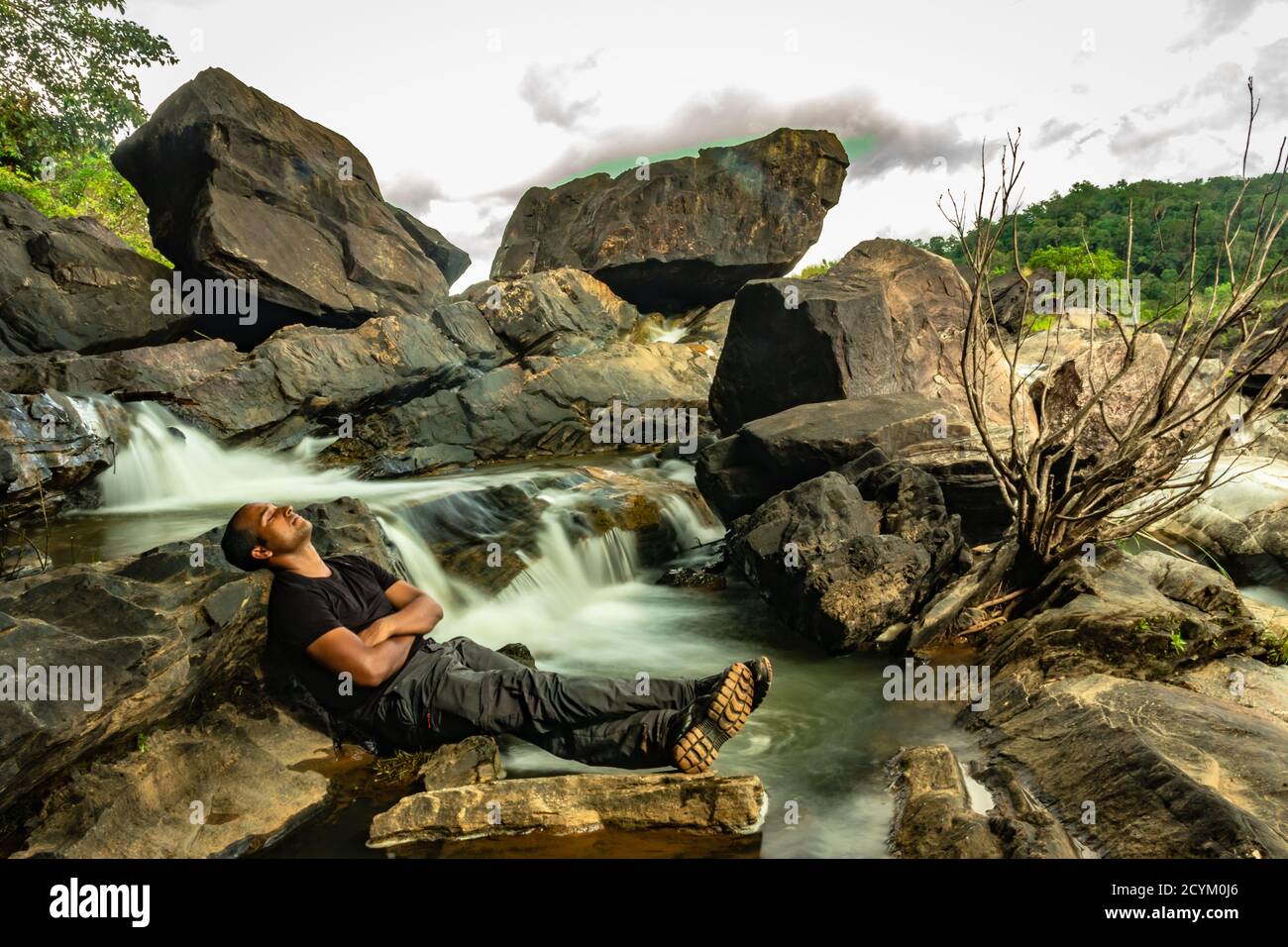 l'uomo che si rilassa nella roccia con la bella cascata flusso lunga esposizione girato alla sera immagine è scattata in remoto ghat foreste occidentali karnataka india. Foto Stock