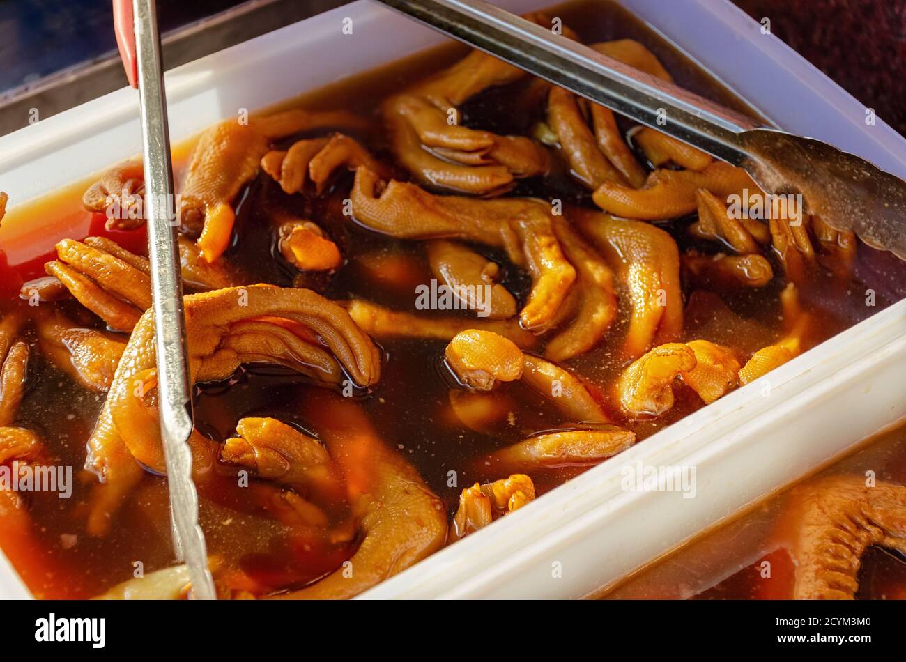 Cibo insolito, strano e disgustoso. Piedi di anatra in salsa o marinata. Cibo di strada in Cina. Immagine sfocata con profondità di campo poco profonda. Foto Stock