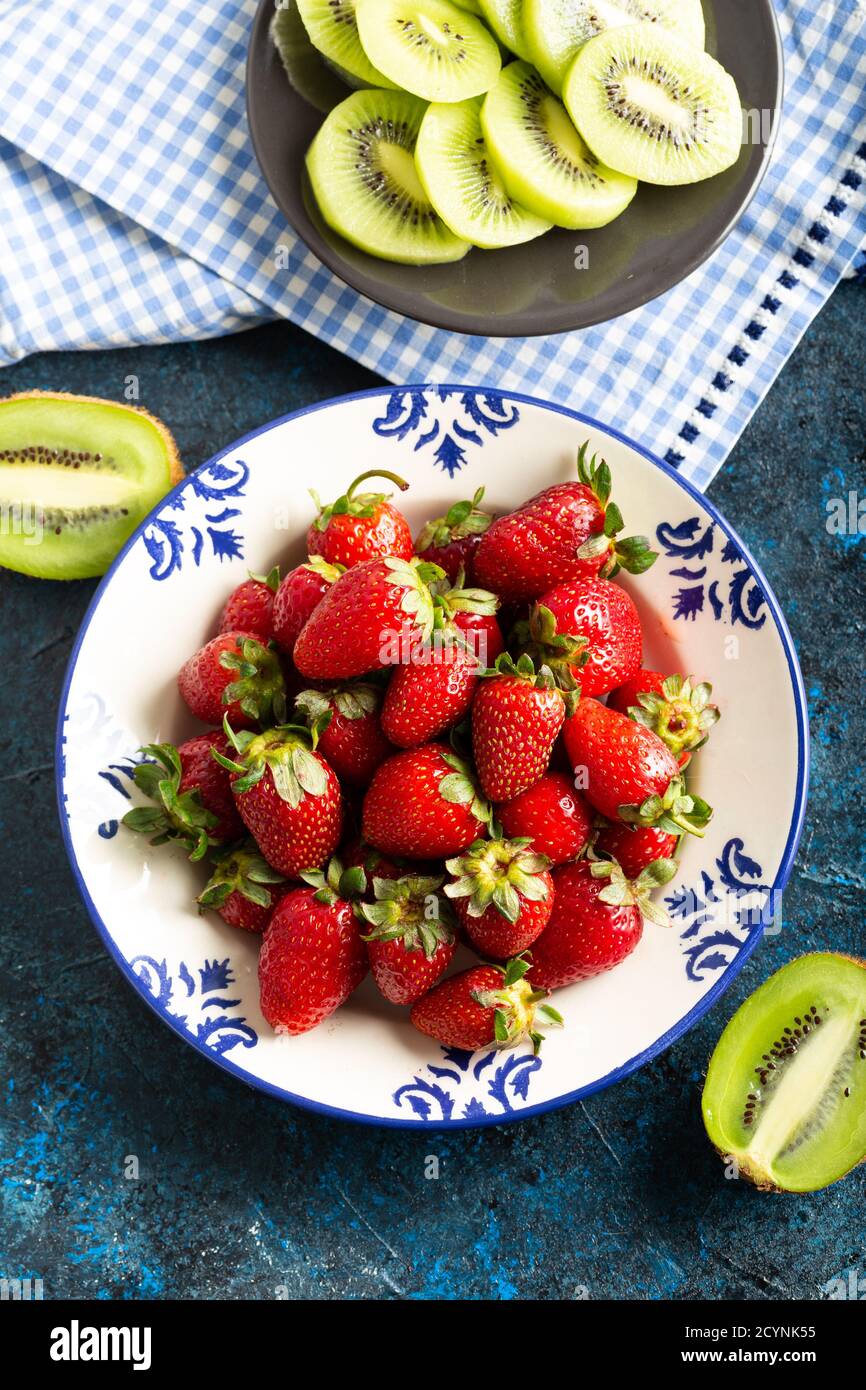 Deliziose fragole rosse in una ciotola bianca, accompagnate da una frutta verde kiwi. Vista dall'alto. Foto Stock