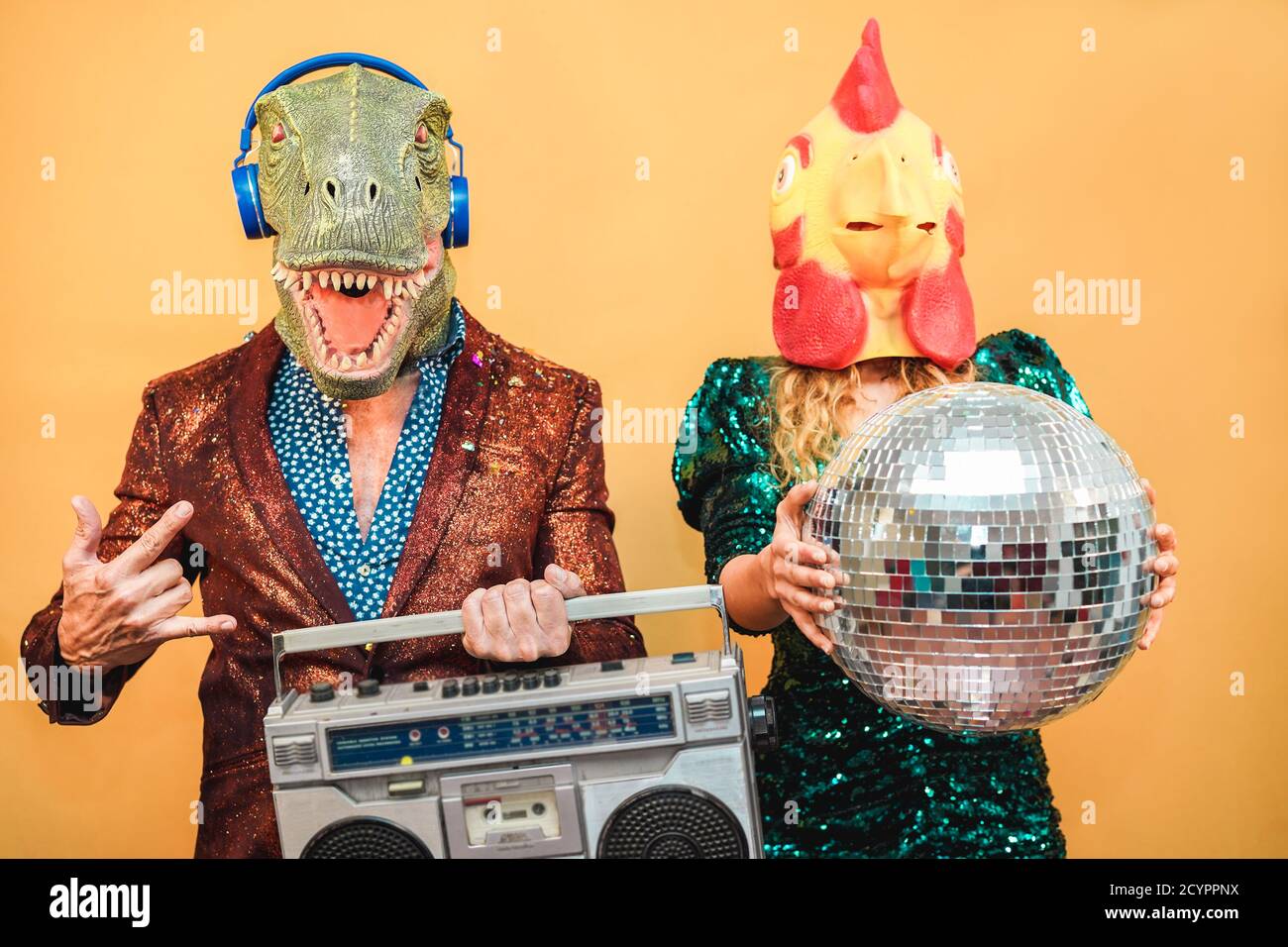 Crazy elegante gente che ascolta musica con stereo boombox vintage - Coppia di moda che indossa t-rex e maschera di pollo al party fest evento - assurdo, holida Foto Stock