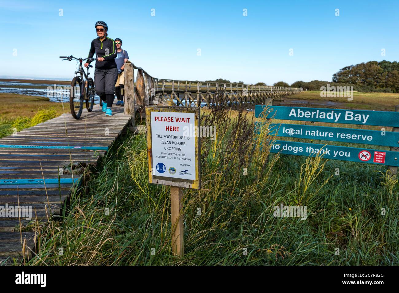 Aberlady Nature Reserve, East Lothian, Scozia, Regno Unito, 2 ottobre 2020. Regno Unito Meteo: Una bella giornata di sole sulla costa. I visitatori devono aderire al sistema di distanziamento sociale a senso unico attraverso lo stretto ponte di legno mentre i ciclisti spingono le biciclette attraverso il ponte Foto Stock