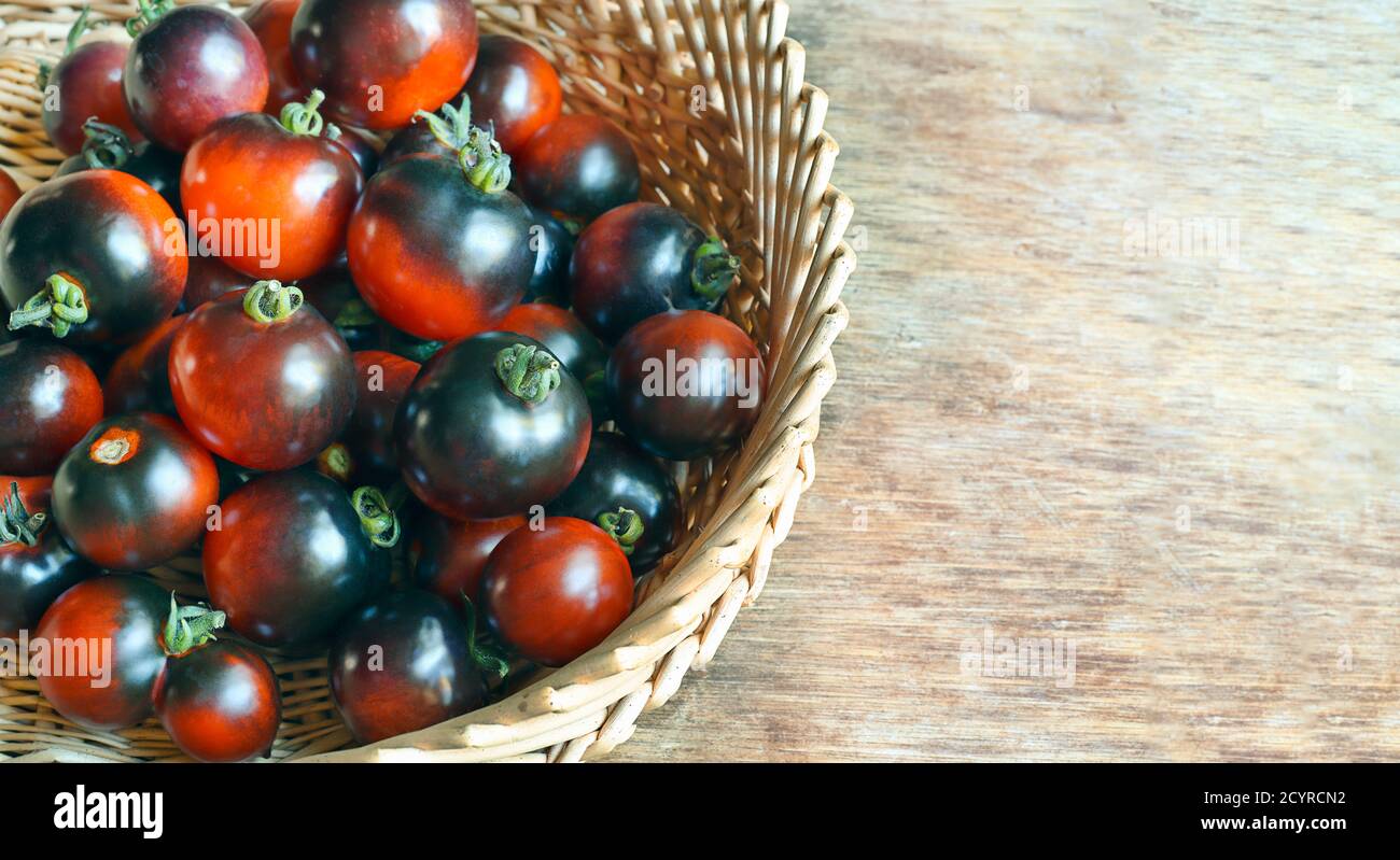 L'indaco matura ha rosa i pomodori neri in un cestino sopra un tavolo di legno Foto Stock