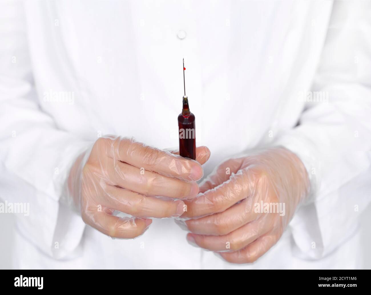 Medico o scienziato di laboratorio in dispositivi di protezione personale che tengono una siringa piena di sangue, con attenzione a gocce singole che fuoriescono dalla punta dell'ago Foto Stock