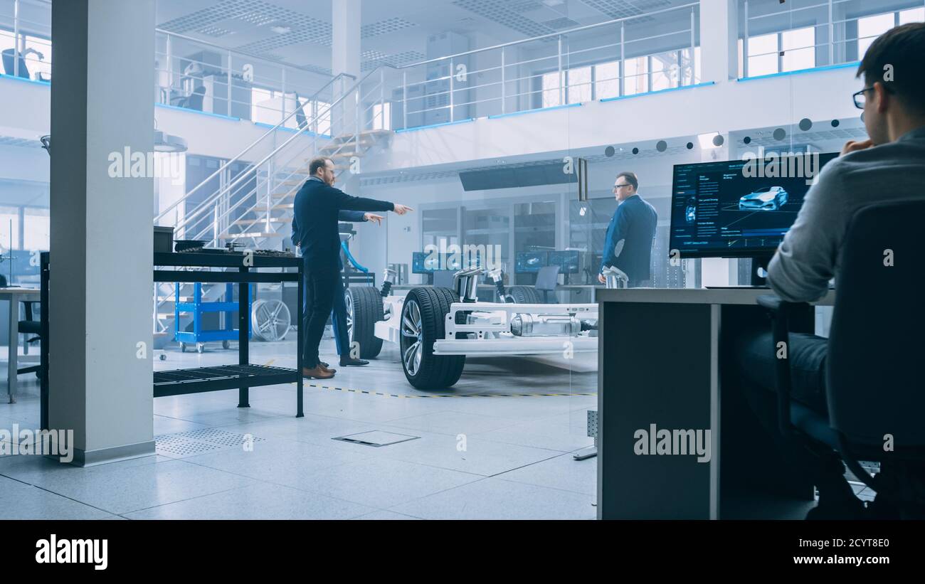Gli ingegneri di progettazione automobilistica parlano mentre lavorano al prototipo del telaio dell'auto elettrica e utilizzano il PC con il software CAD. Laboratorio innovativo Foto Stock