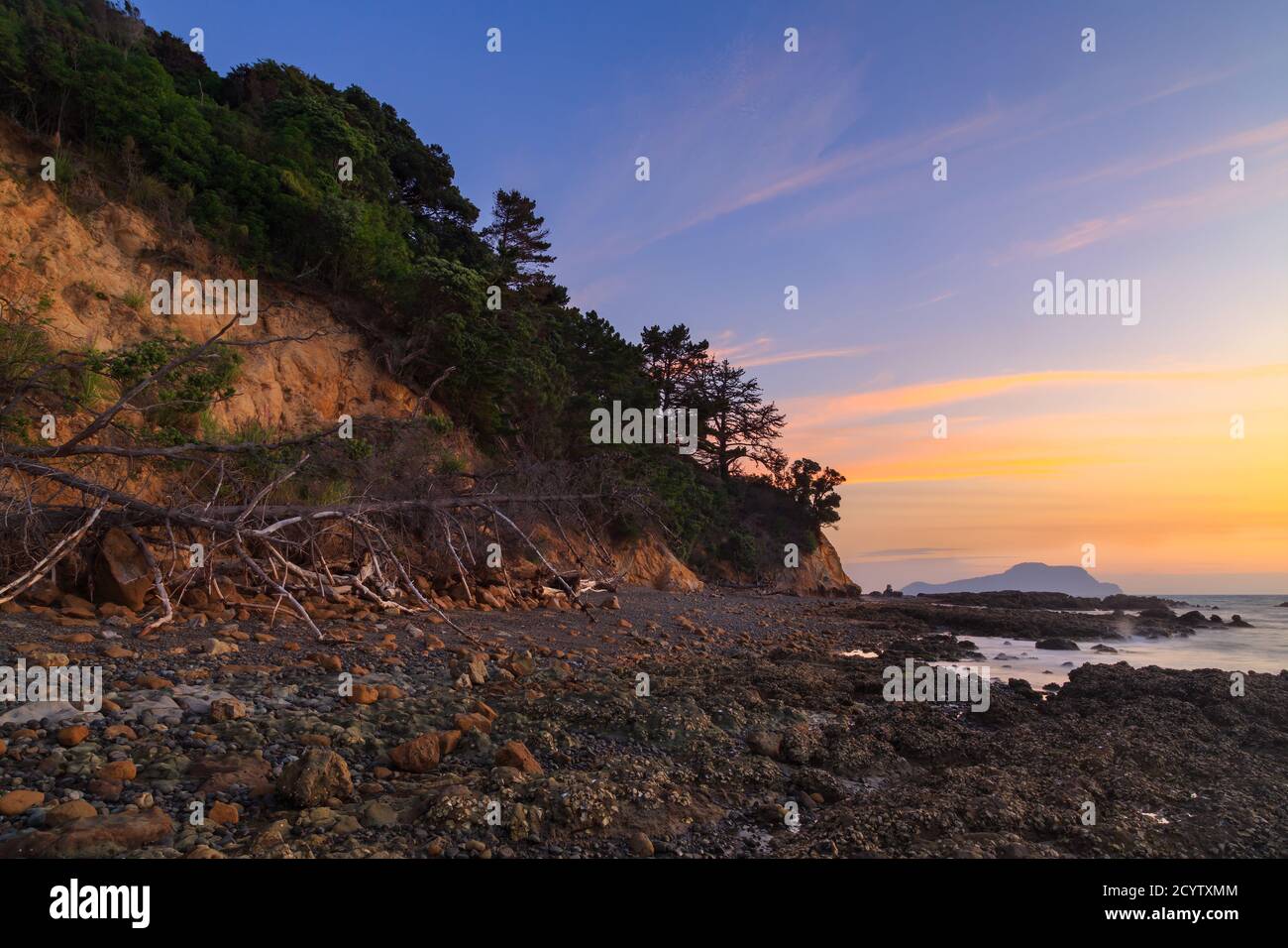 Un bel cielo di tramonto sopra una spiaggia sassosa e scogliere costiere. Presa sulla penisola di Coromandel, Nuova Zelanda Foto Stock