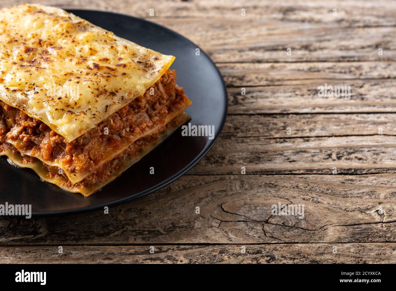 Pezzo di lasagne di carne su piastra nera su legno rustico tabella Foto Stock