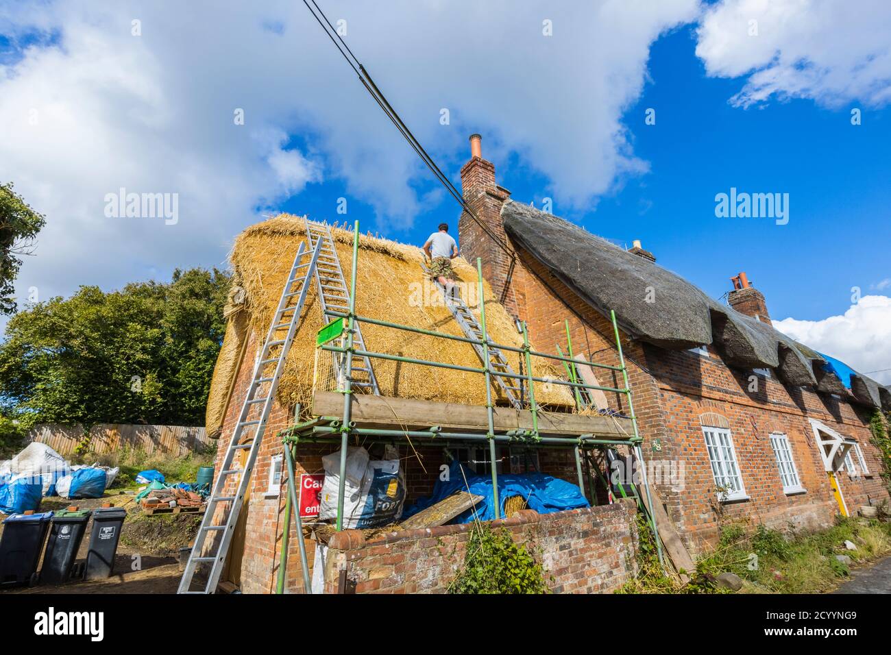 Un thatcher esperto al lavoro che sostituisce il tetto tradizionale di paglia di un vecchio cottage in Great Bedwyn, un villaggio nel Wiltshire orientale, Inghilterra meridionale Foto Stock