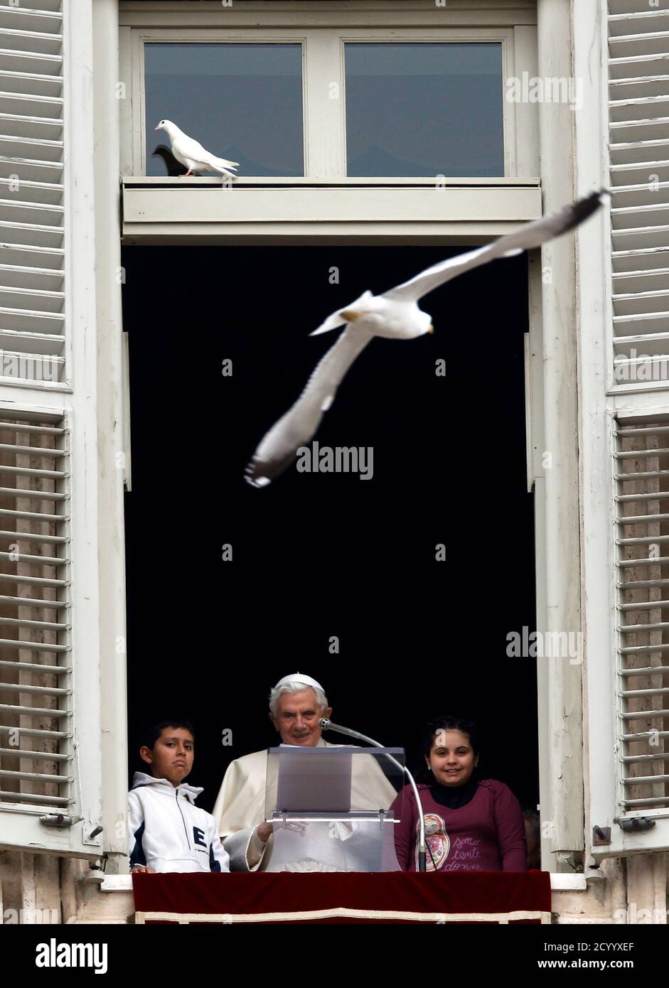 Pope Benedict XVI and two young members of "Azione Cattolica" (Catholic Action movement) look on as a seagull (top R) flies after he released doves from a window of his private apartments while leading the Angelus prayer in Saint Peter's Square at the Vatican January 29, 2012. REUTERS/Alessandro Bianchi (VATICAN - Tags: RELIGION) Foto Stock