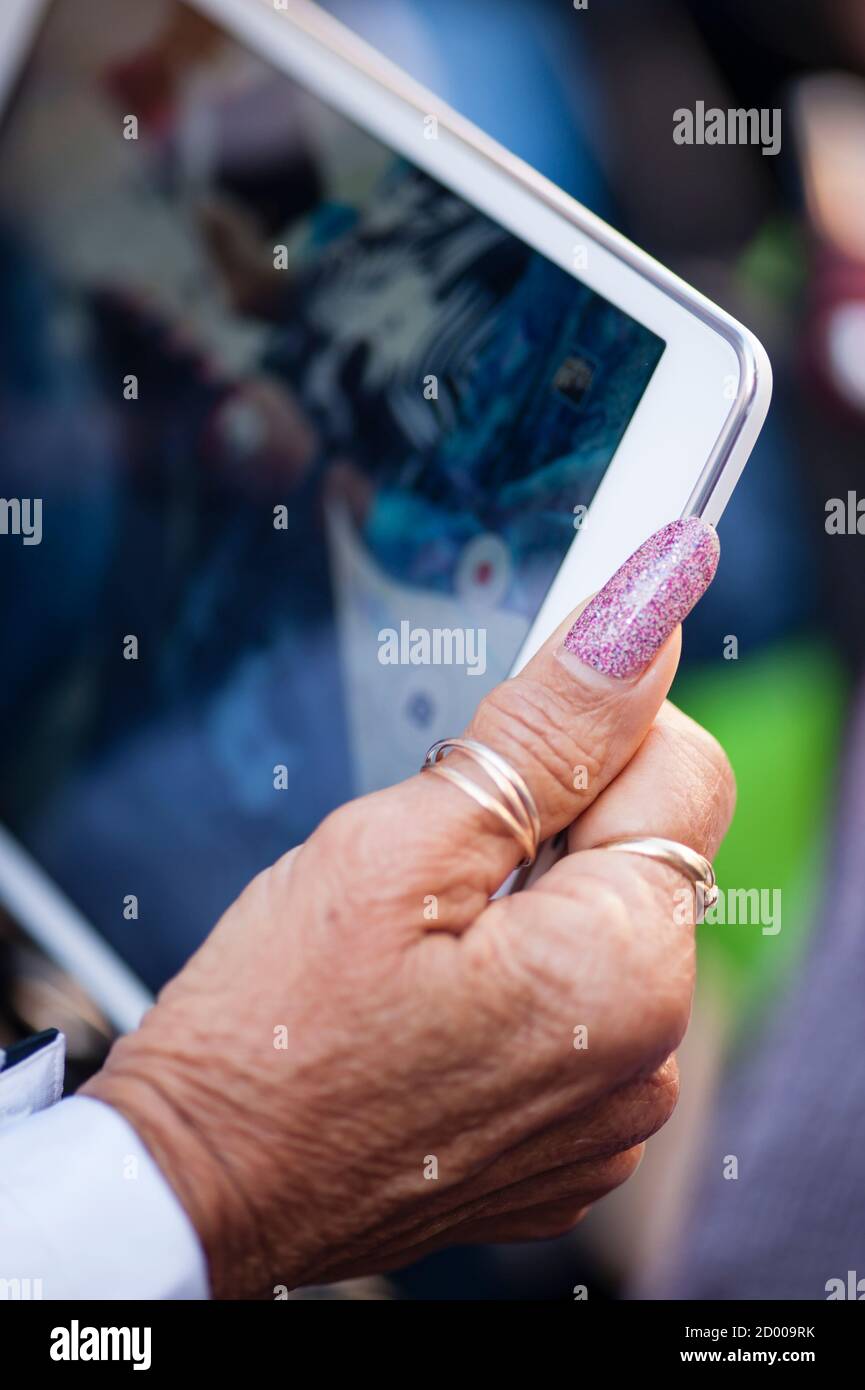 Mano da donna anziana con anelli e lungo chiodo per pollice lucidato reggendo la compressa Foto Stock