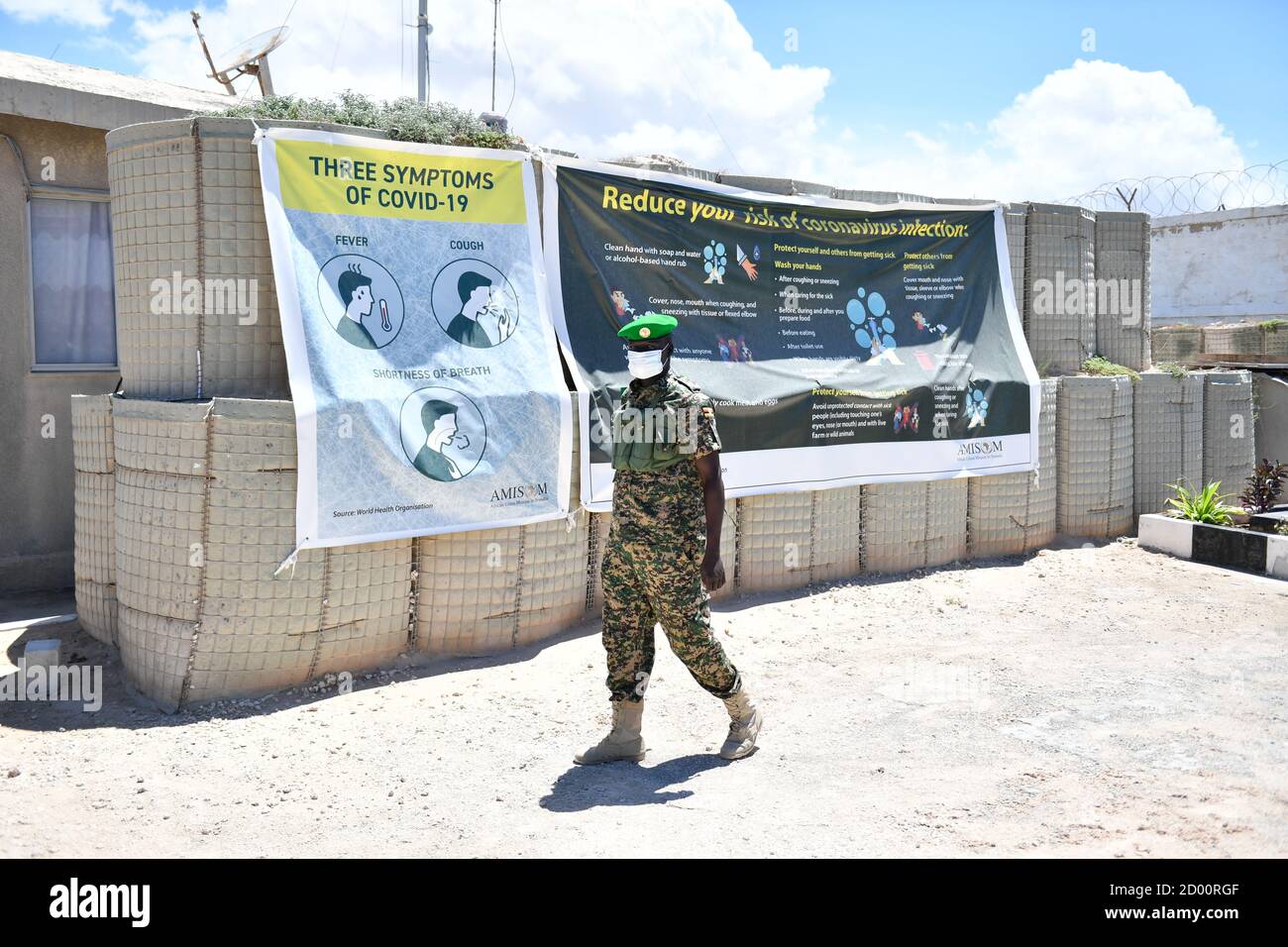 Il 26 aprile 2020, un soldato ugandese AMISOM passa davanti a uno striscione di sensibilizzazione Covid-19 presso il quartier generale del settore uno a Mogadiscio, Somalia, sottolineando l'importanza dei protocolli sanitari nelle missioni di mantenimento della pace. Foto Stock