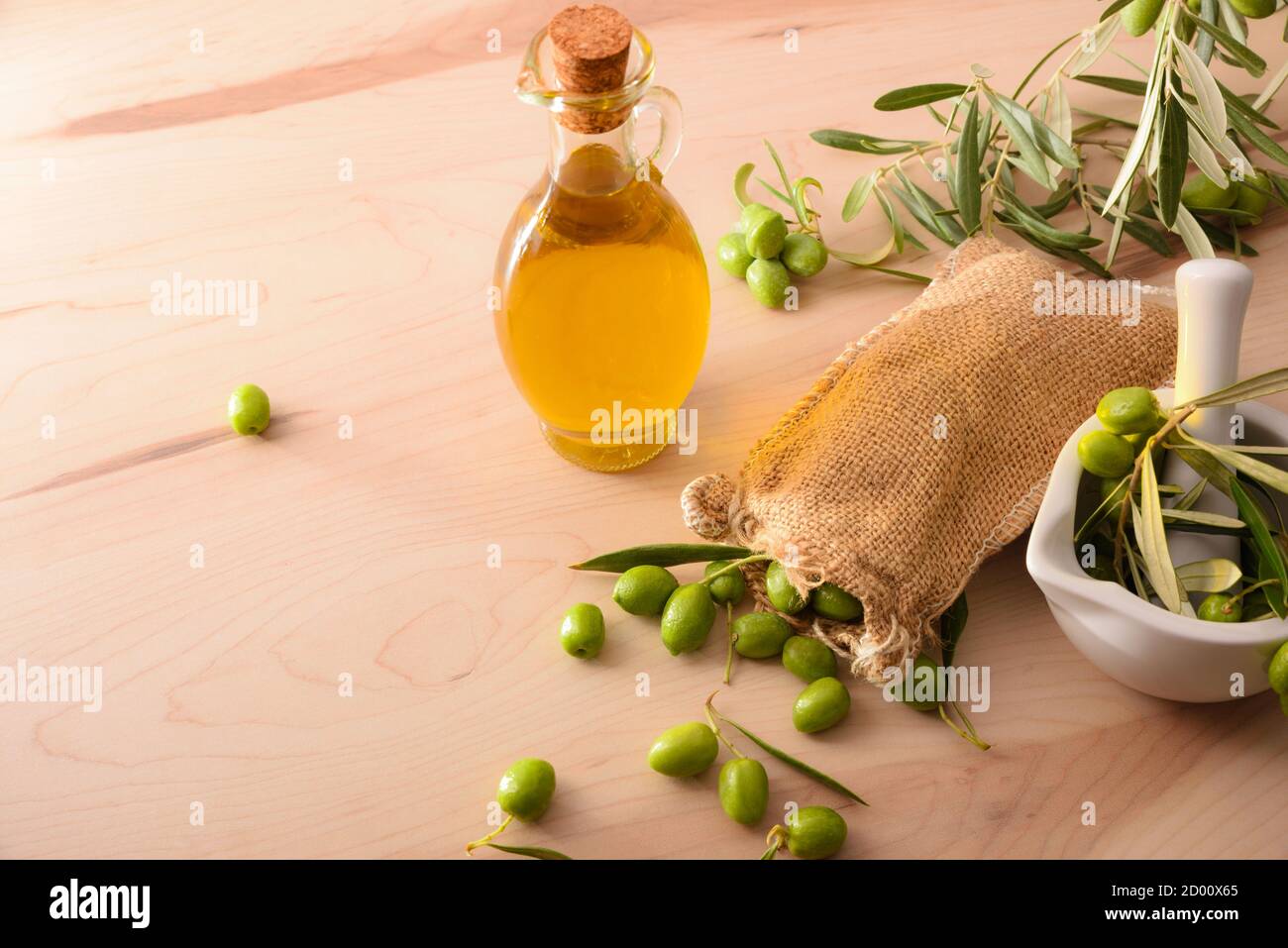 Preparazione dell'olio d'oliva in vetro ceramico per la cura del corpo e della cucina a tavola con Malta e sacco di olive. Vista rialzata. Foto Stock