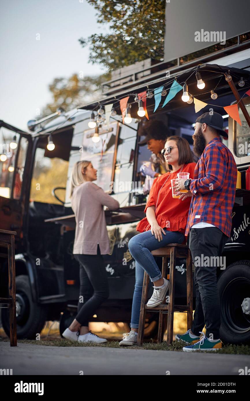 Gli amici si rilassano con la birra davanti al camion del cibo Foto Stock