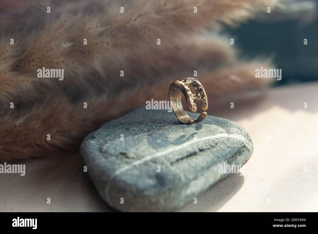 anello trendy in ottone pressofuso vintage. anello da donna di gioielli astratto disegno primo piano su una pietra grigia naturale con shadows Foto Stock