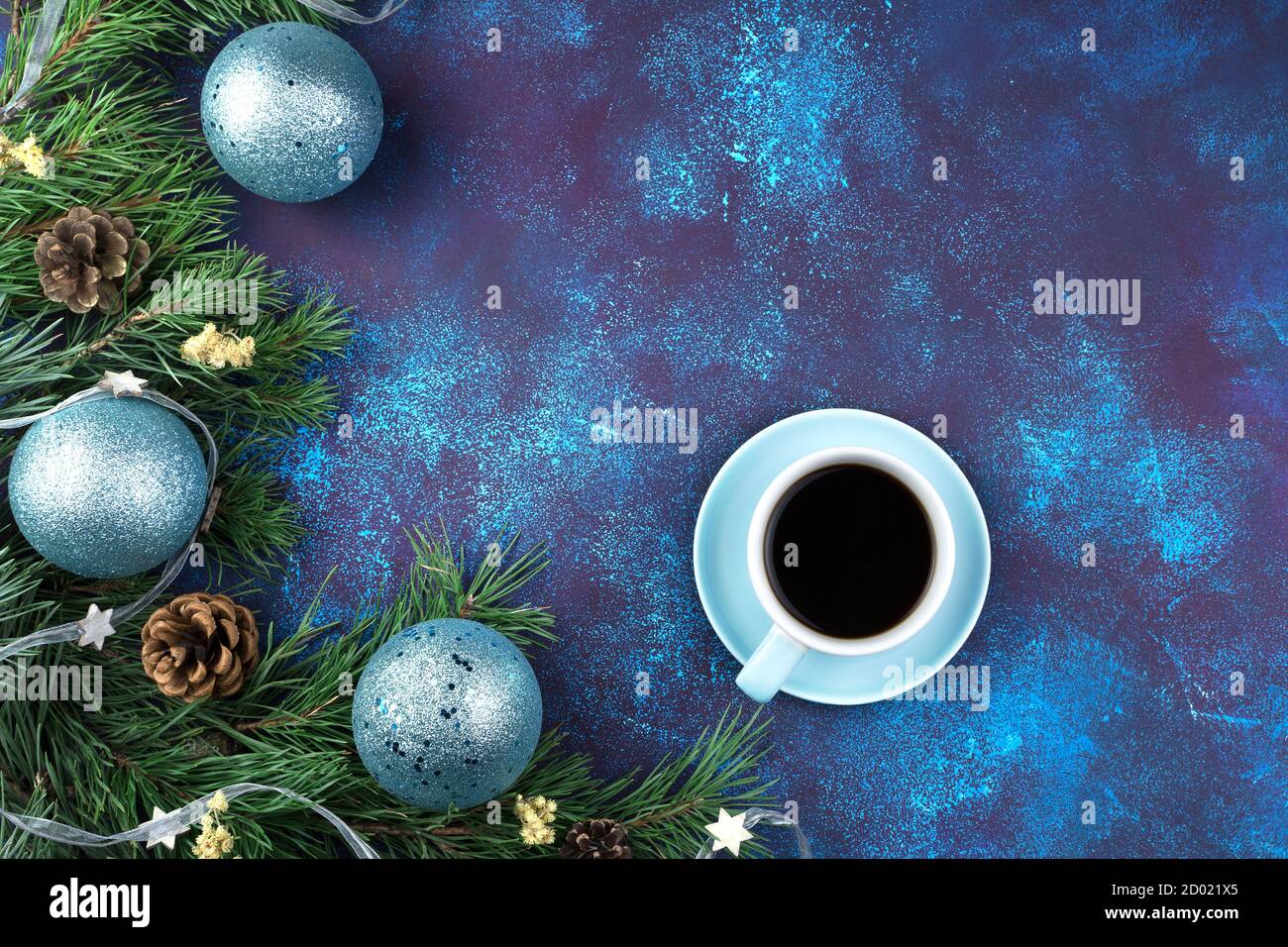 Composizione di Natale con una tazza di caffè su un piatto blu, rami di pino con palle di Natale e giocattoli su sfondo blu. Foto Stock