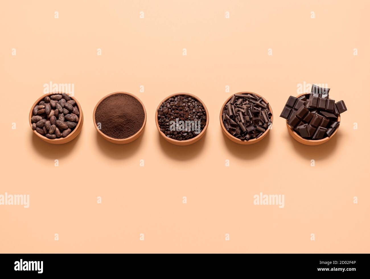 Ingredienti di cioccolato, fagioli di cacao, polvere di cacao, pezzi di cioccolato in ciotole, isolati su sfondo beige. Piatto con cacao e cioccolato fondente. Foto Stock