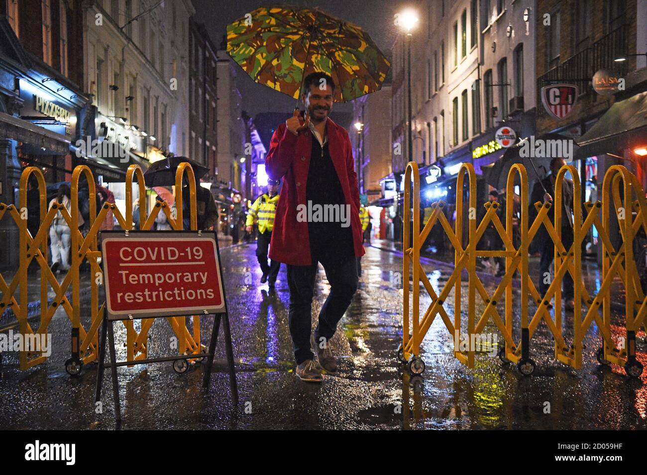 La gente coraggiosa la forte pioggia a Soho, Londra, davanti ai pub e ristoranti del coprifuoco alle 22:00 sono soggetti a per combattere l'aumento dei casi di coronavirus in Inghilterra. Foto Stock