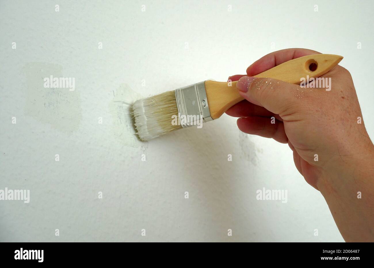 Un uomo sta dipingendo una parete di colore bianco con un pennello. Sta migliorando la sua casa, rimuovendo le macchie sul muro. Lavora in movimenti delicati. Foto Stock