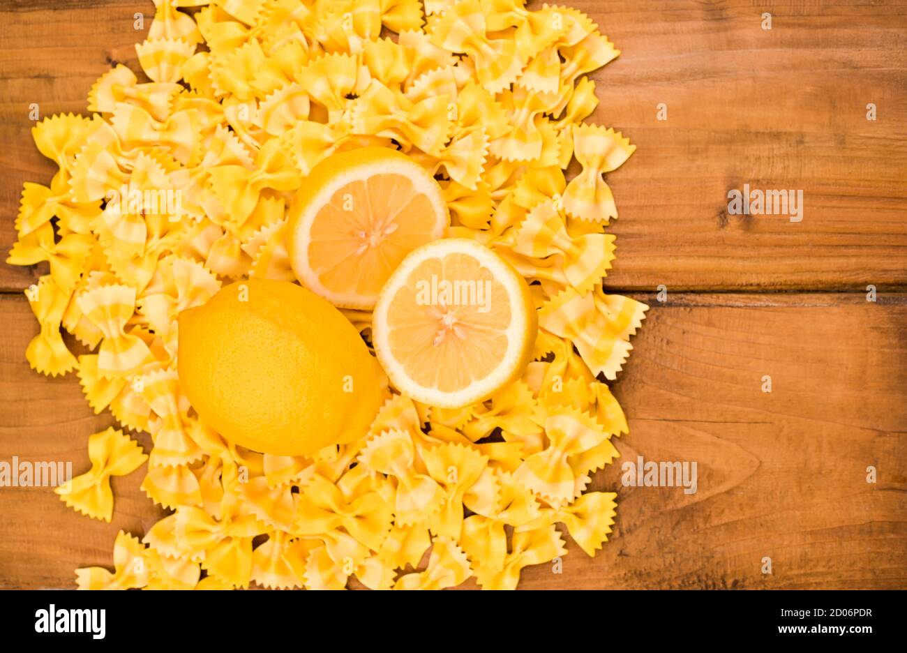 Pasta secca farfalle e limoni su sfondo ligneo. Pasta colorata, cucina tipica italiana del sud. Vista dall'alto. Foto di alta qualità. Spazio libero per il testo Foto Stock