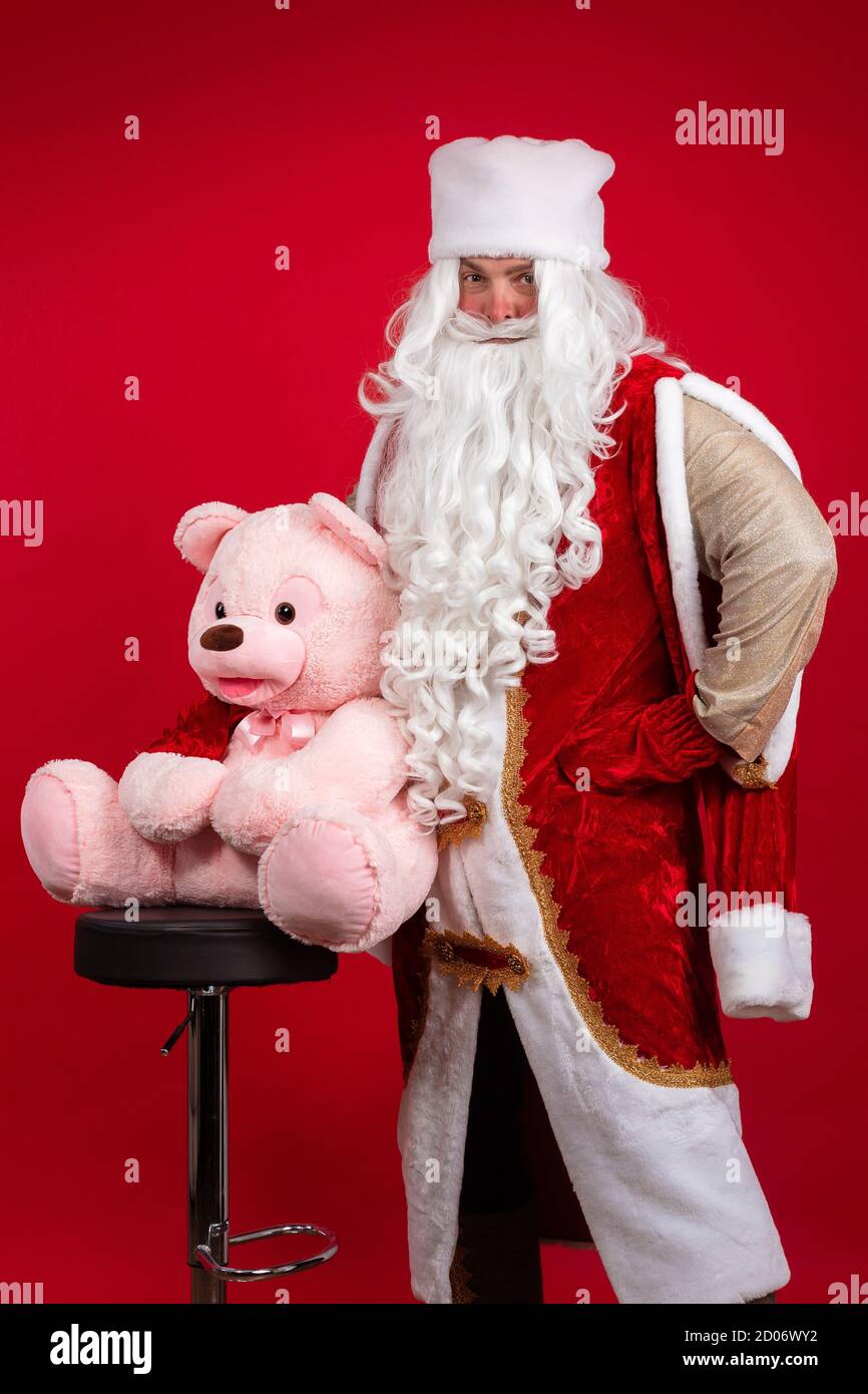 Babbo Natale emozionale con una lunga barba bianca in un cappotto rosso e cappello  bianco in posa con un grande orsetto rosa Foto stock - Alamy