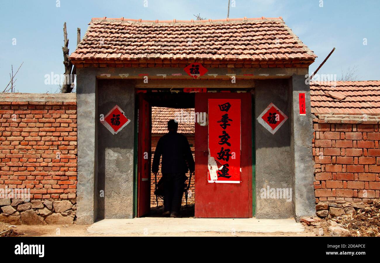 Un agricoltore anziano spinge una carriola attraverso la porta della sua  casa, che ha il carattere cinese 'buona fortuna' incollato sulle pareti,  situato alla periferia della città di Zhucheng nella provincia di