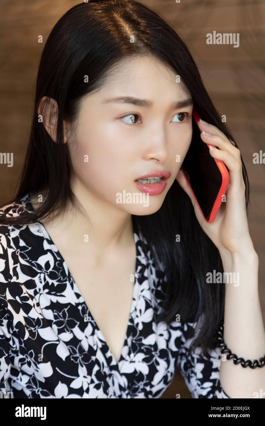 Molto sorprendo la donna cinese americana che usa uno smartphone rosso in una caffetteria Foto Stock