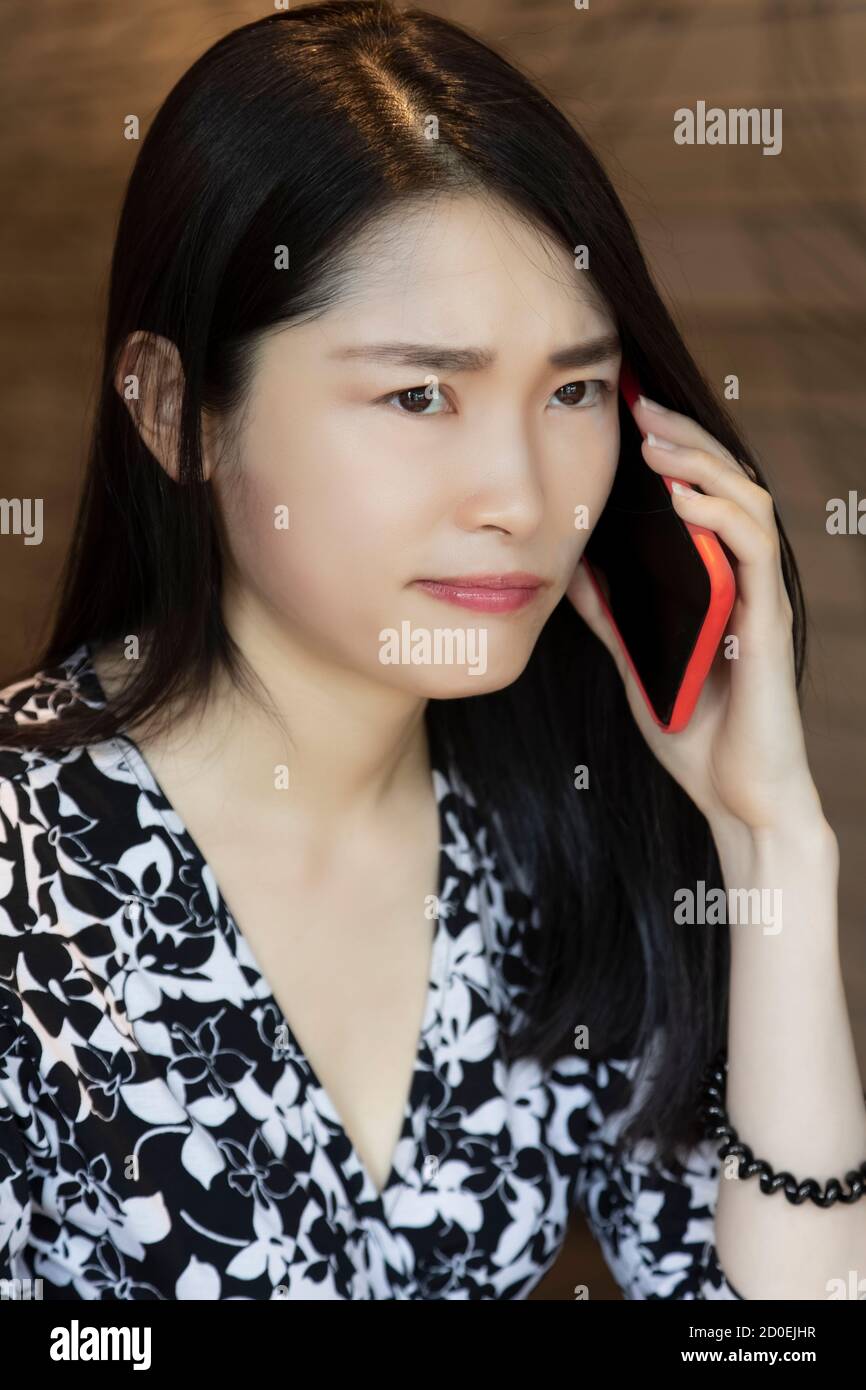 Donna americana cinese nel profondo del pensiero utilizzando un rosso intelligente telefono in una caffetteria Foto Stock