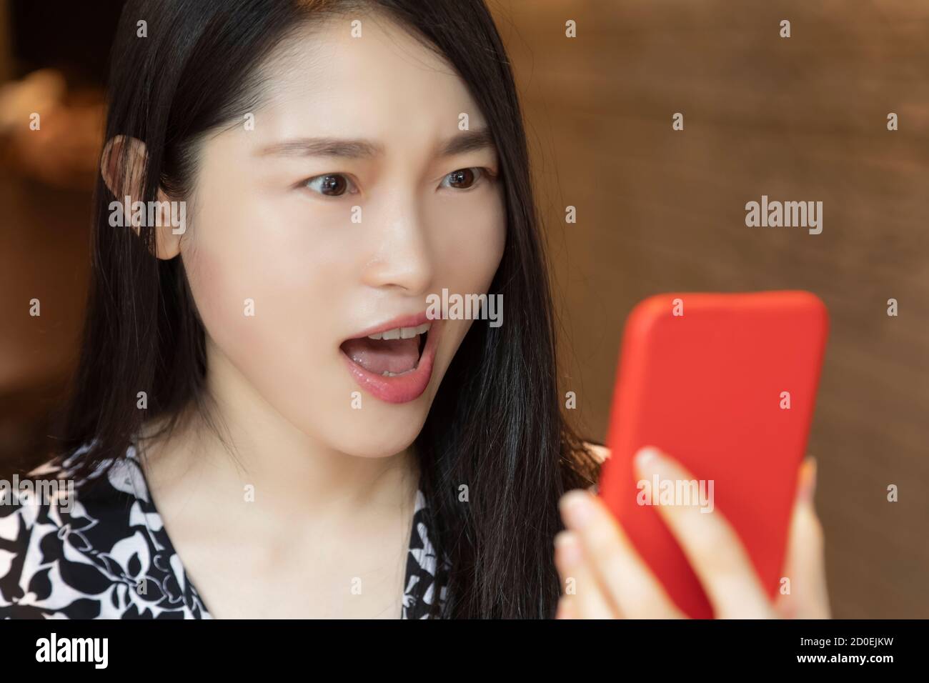 Molto sorprendo la donna cinese americana che usa uno smartphone rosso in una caffetteria Foto Stock