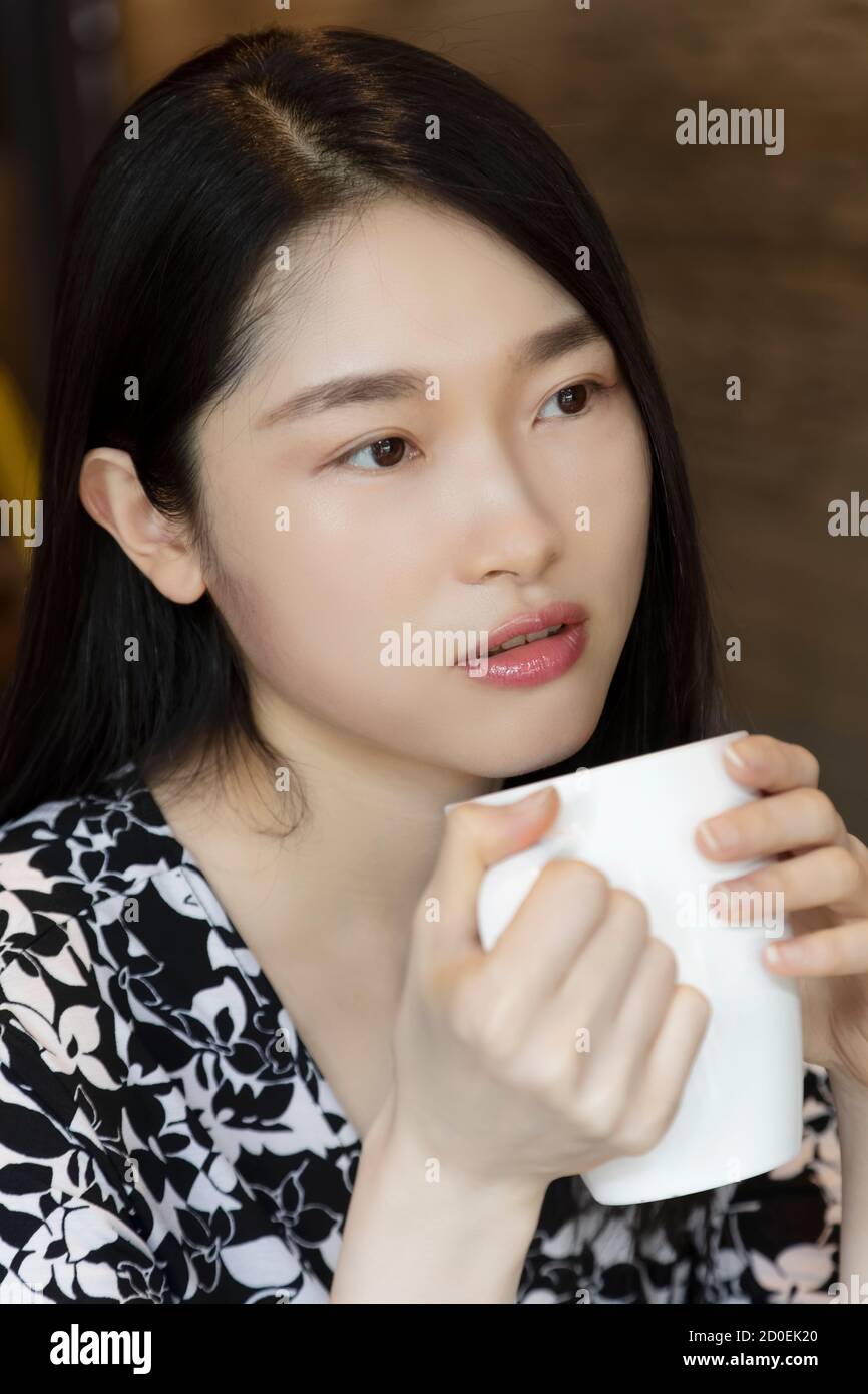 Donna americana cinese che tiene una tazza di caffè in un caffetteria con area fotocopie Foto Stock