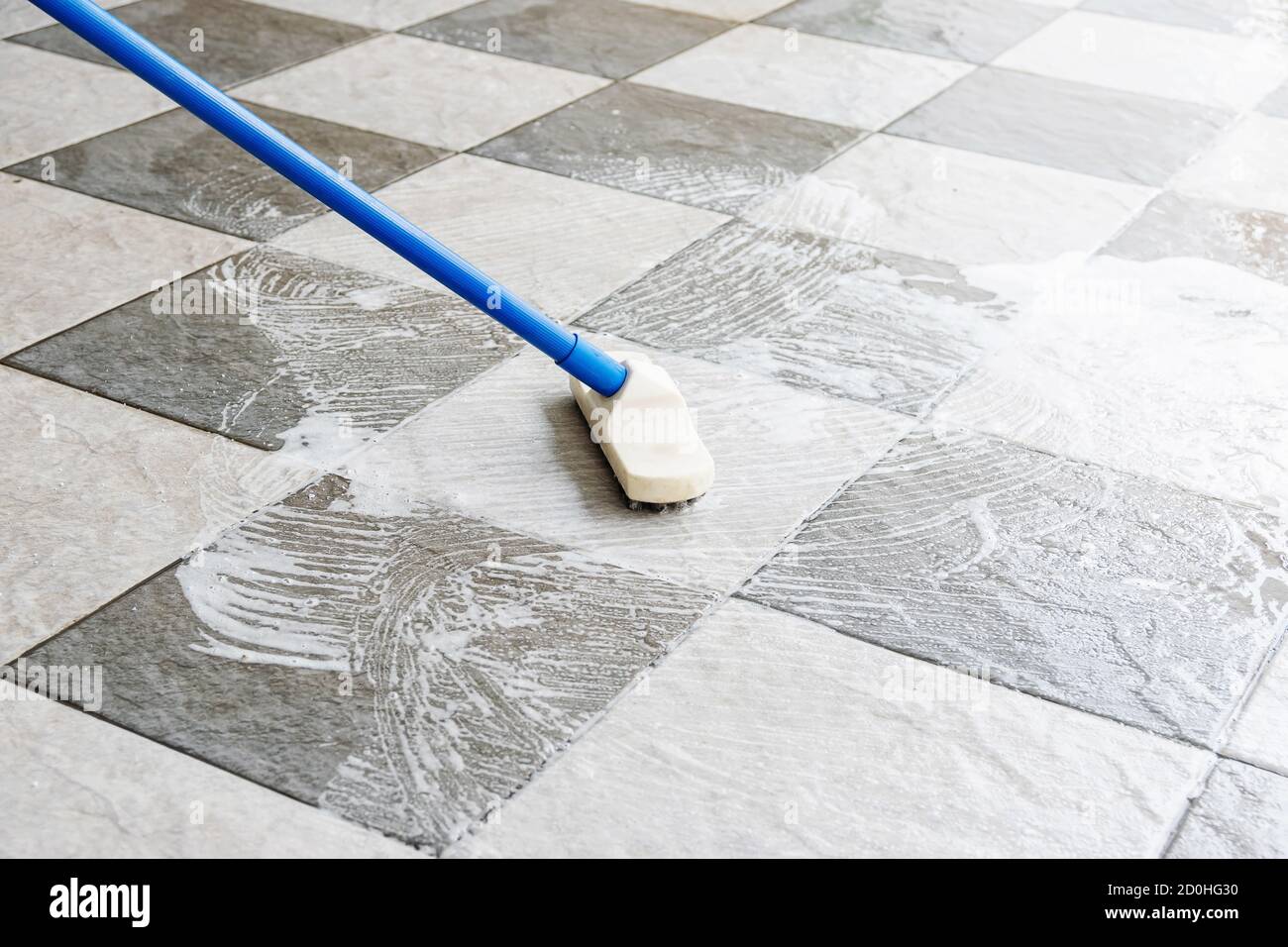 Pulire il pavimento delle piastrelle con una spazzola per pavimenti a manico lungo. Foto Stock