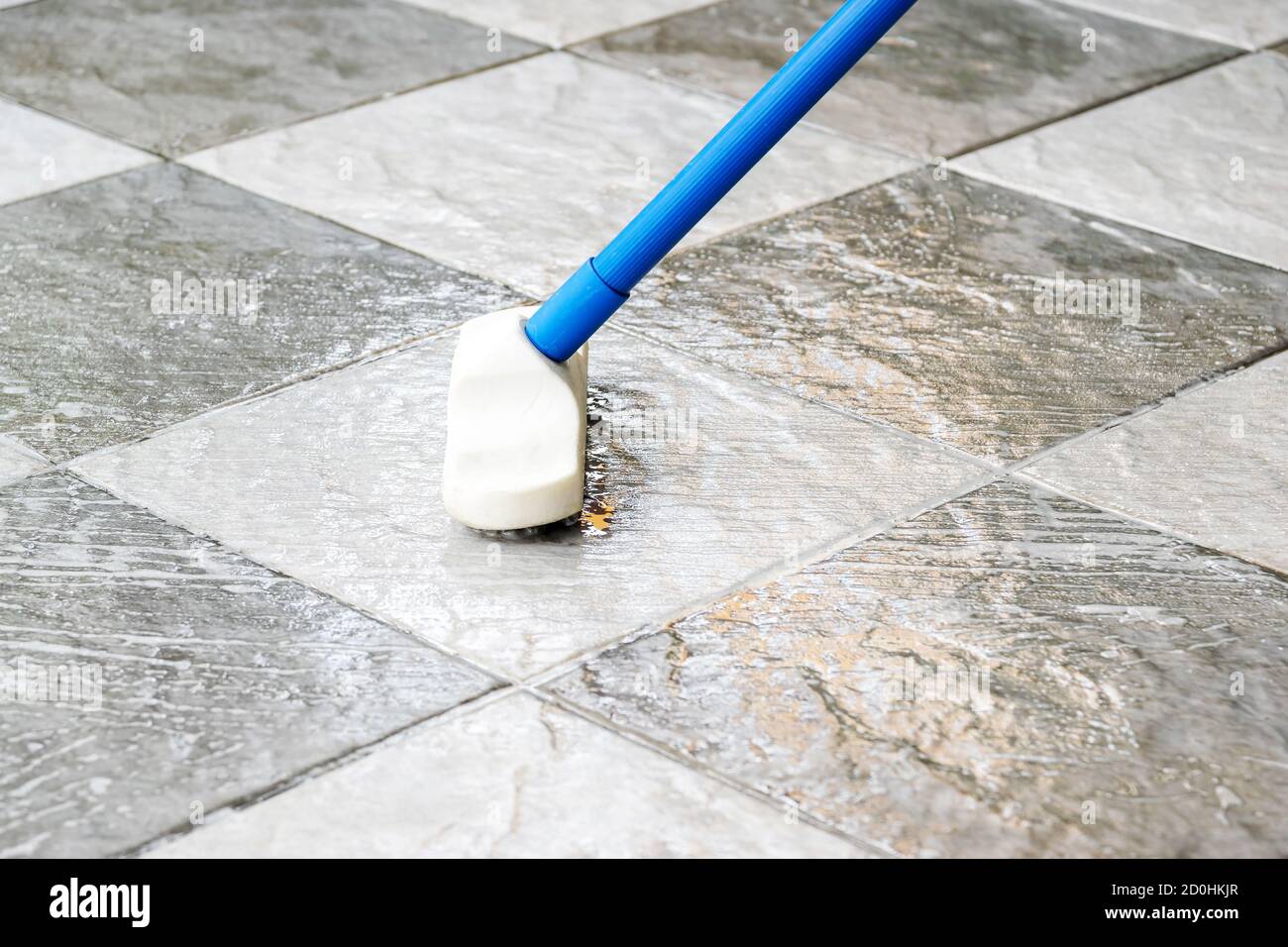 Pulire il pavimento delle piastrelle con una spazzola per pavimenti a manico lungo. Foto Stock