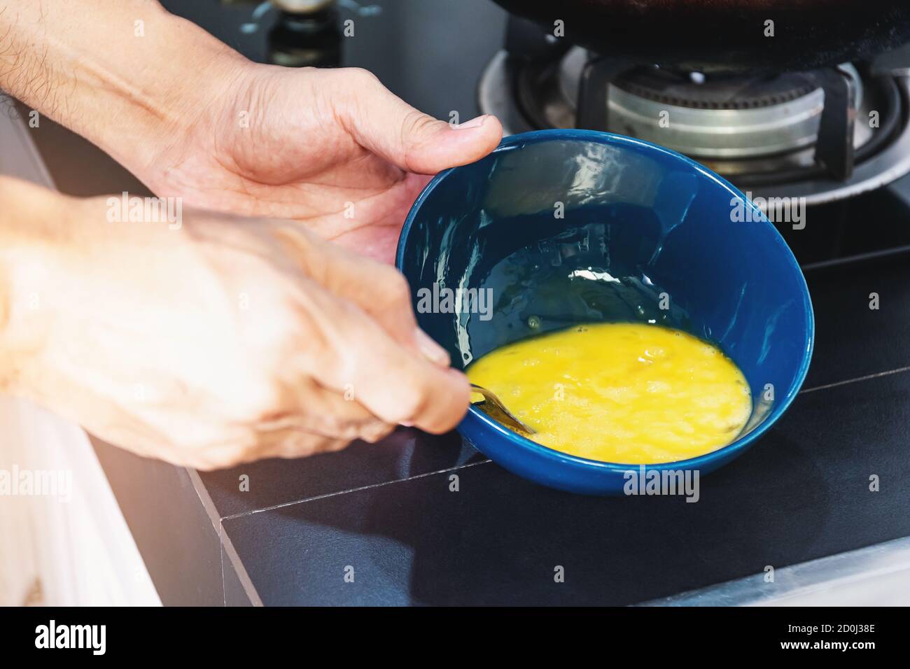 Chiudete la mano degli uomini con un cucchiaio sbattete le uova in una tazza di ceramica per cucinare. Foto Stock