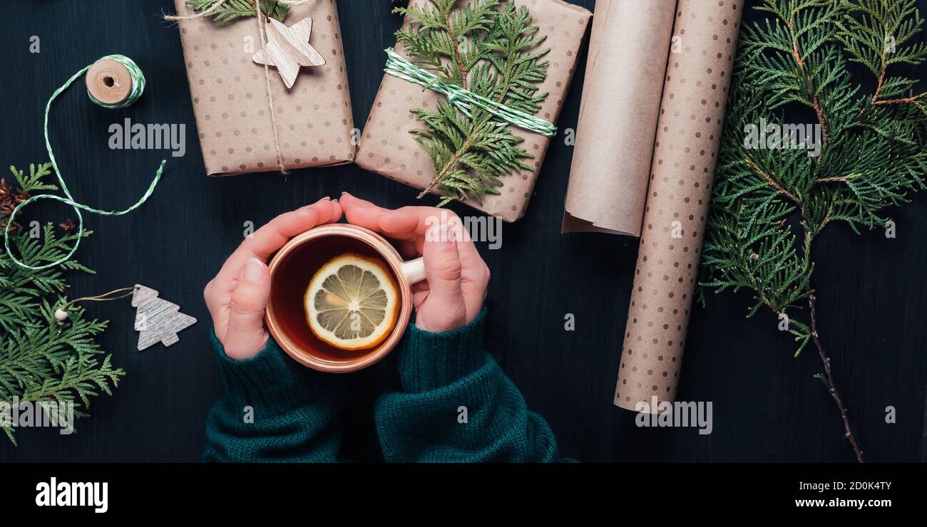 Scatole regalo di Natale avvolte in carta kraft e decorare con rami di cipresso su rustico sfondo di legno. Tazza da donna con tè. Vista dall'alto Foto Stock