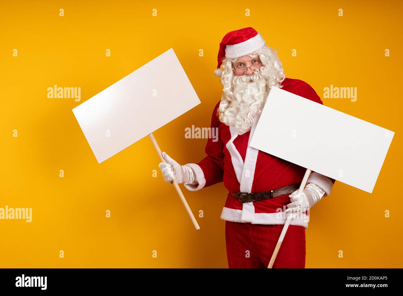 Attore maschile emotivo in un costume di Babbo Natale tiene nelle sue mani  due grandi cartelloni bianchi su un bastone per registrare annunci e posare  su un bac giallo Foto stock -
