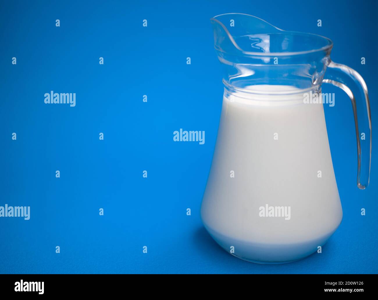 Un litro di latte in una caraffa di vetro su sfondo blu Foto Stock