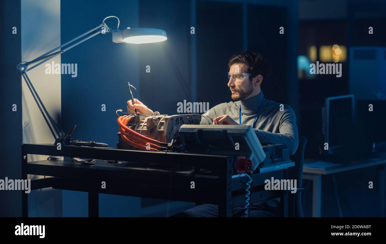 L'ingegnere automobilistico professionista in occhiali e attrezzi di ispezione sta testando un motore elettrico usato in un laboratorio high tech di notte. Foto Stock