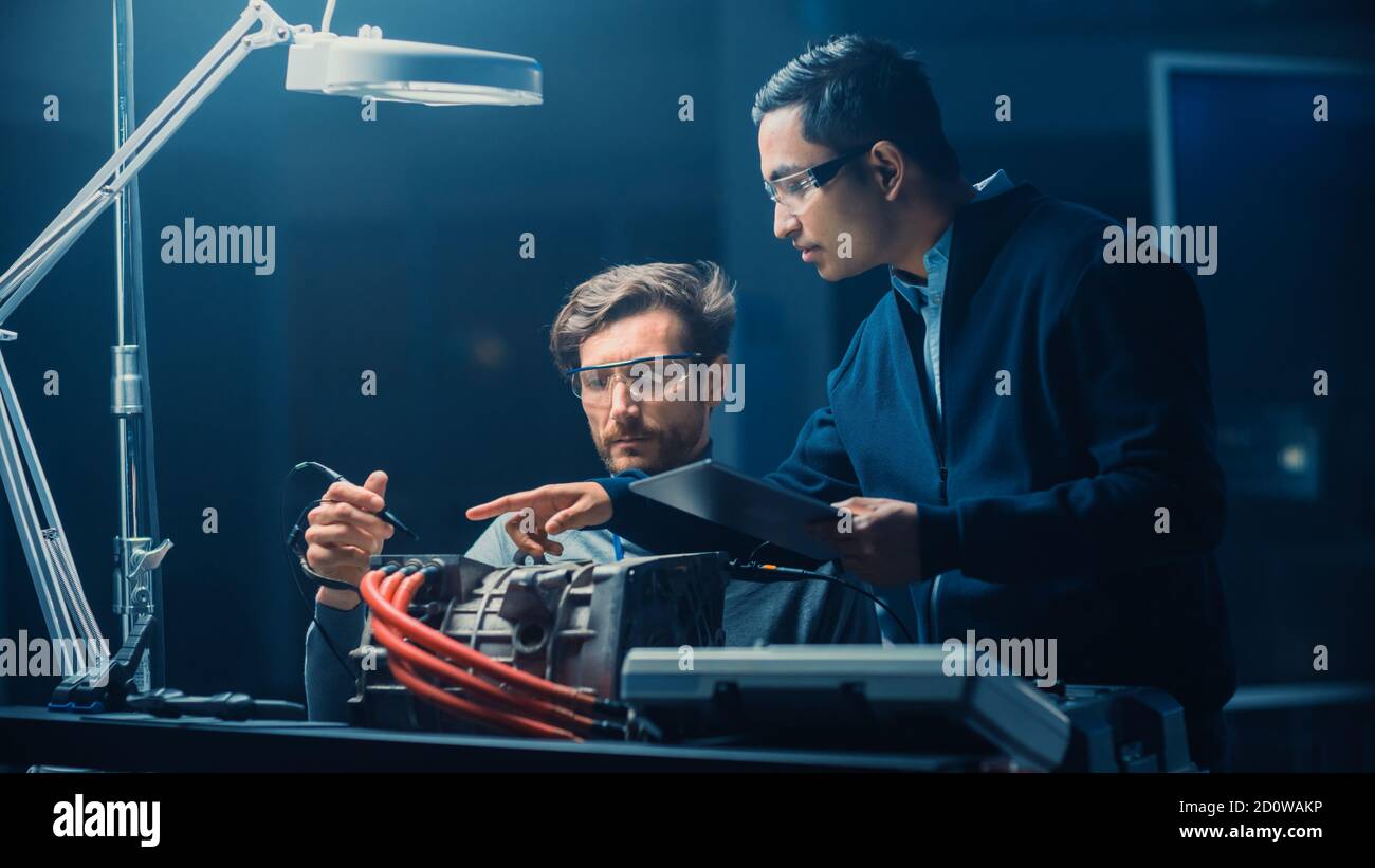 Due ingegneri automobilistici professionisti con un computer tablet e ispezione Gli attrezzi stanno avendo una conversazione mentre testano un motore elettrico In alto Foto Stock