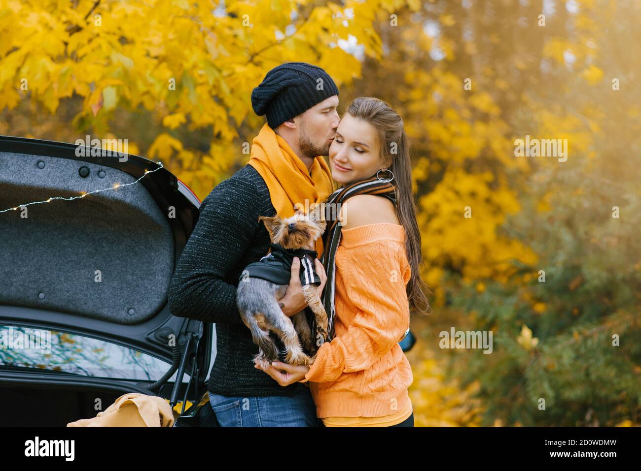 Un ragazzo e una ragazza in amore abbraccio in un parco autunnale, un ragazzo tiene un cane carino tra le sue braccia e bacia la sua ragazza preferita Foto Stock