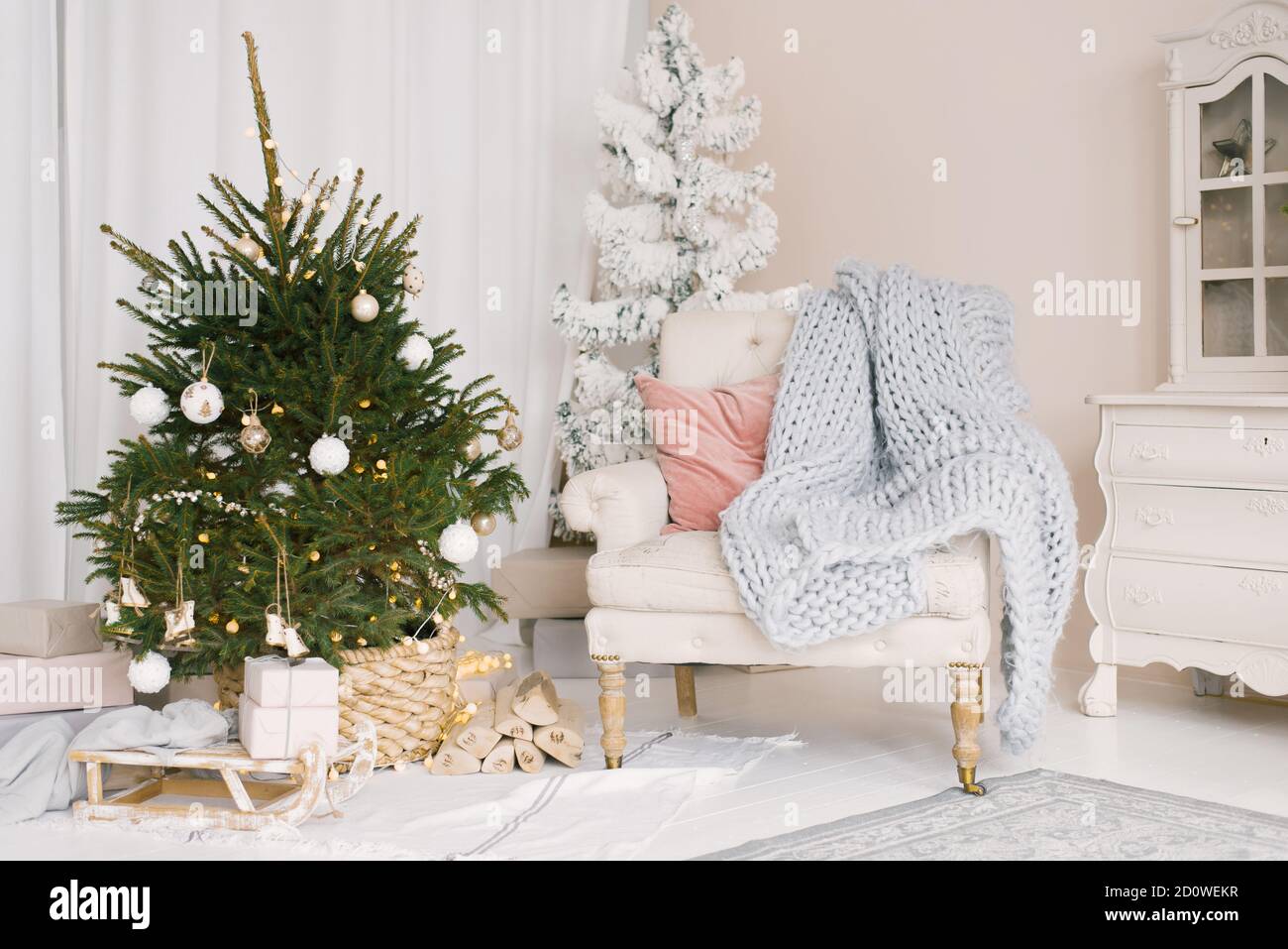 Slitta di Natale con regali e una coperta, una sedia con cuscini vicino all'albero di Natale nel soggiorno, decorato per il nuovo anno Foto Stock