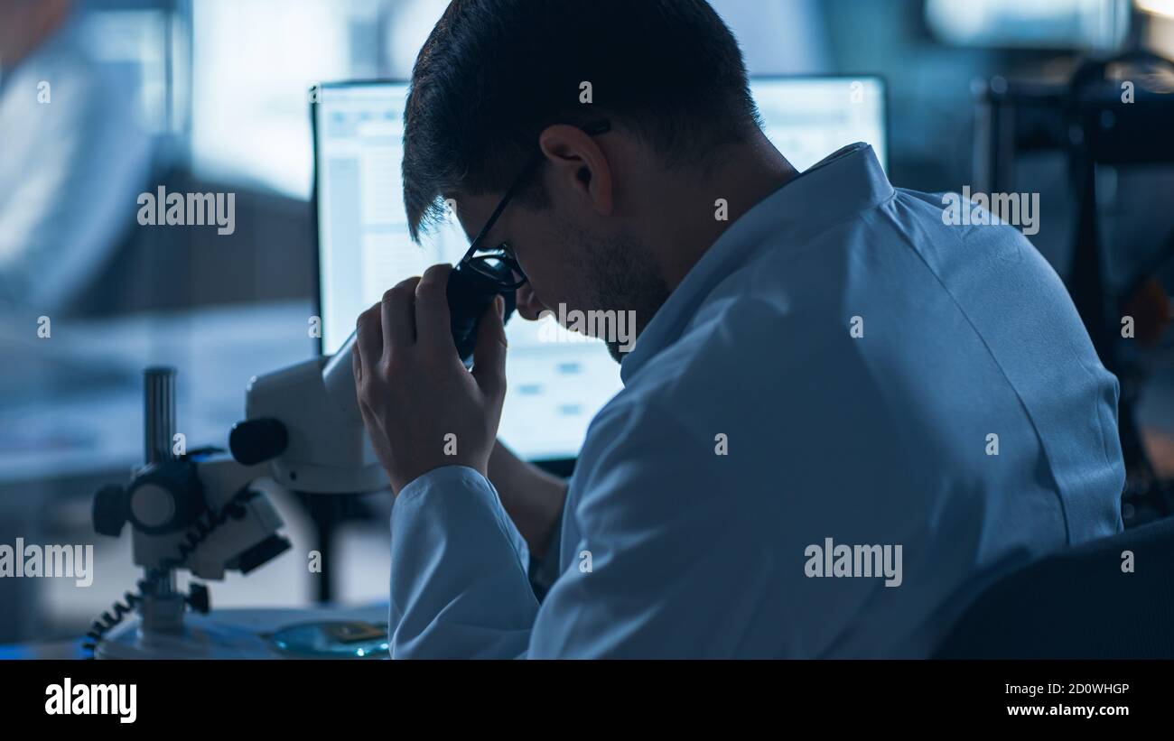 Shot of a Male IT Scientist utilizza un computer con microscopio elettronico. Nel background Technology Development Laboratory con scienziati, ingegneri Foto Stock