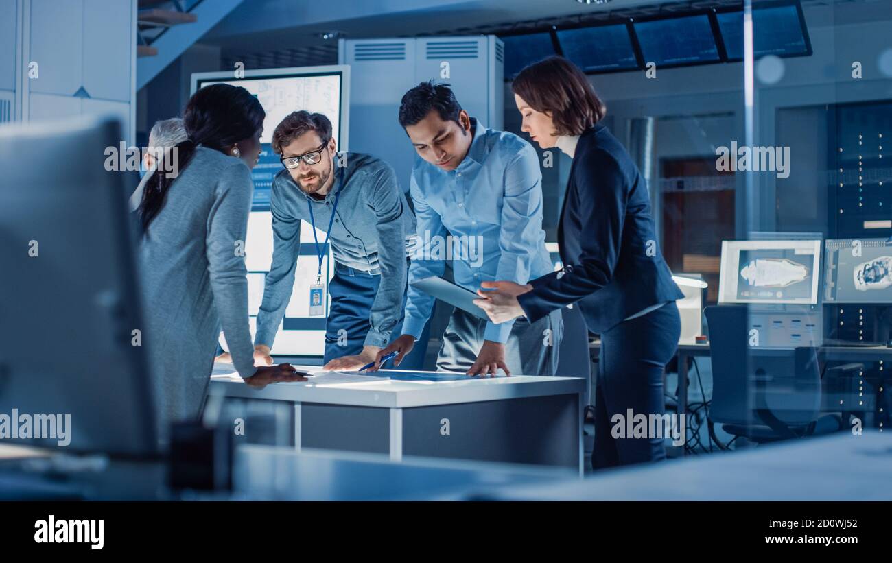 Incontri di ingegneri nel laboratorio di Ricerca tecnologica: Ingegneri, scienziati e sviluppatori si sono riuniti intorno illuminato tavolo da conferenza, parlare e. Foto Stock