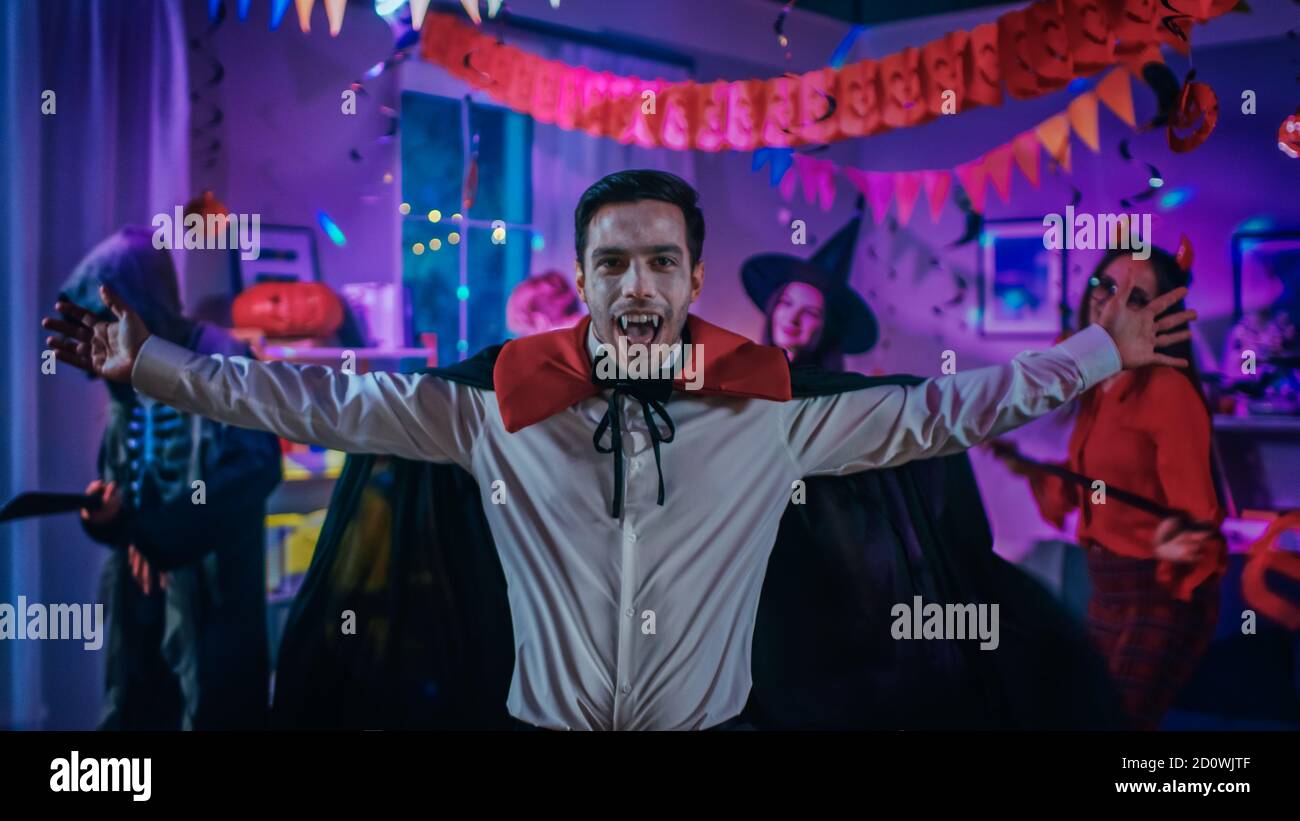 Halloween Costume Party: Conte Dracula indossare il suo capo fa Vampire Dance, in background bella strega, splendida lei diavolo e paura Foto Stock