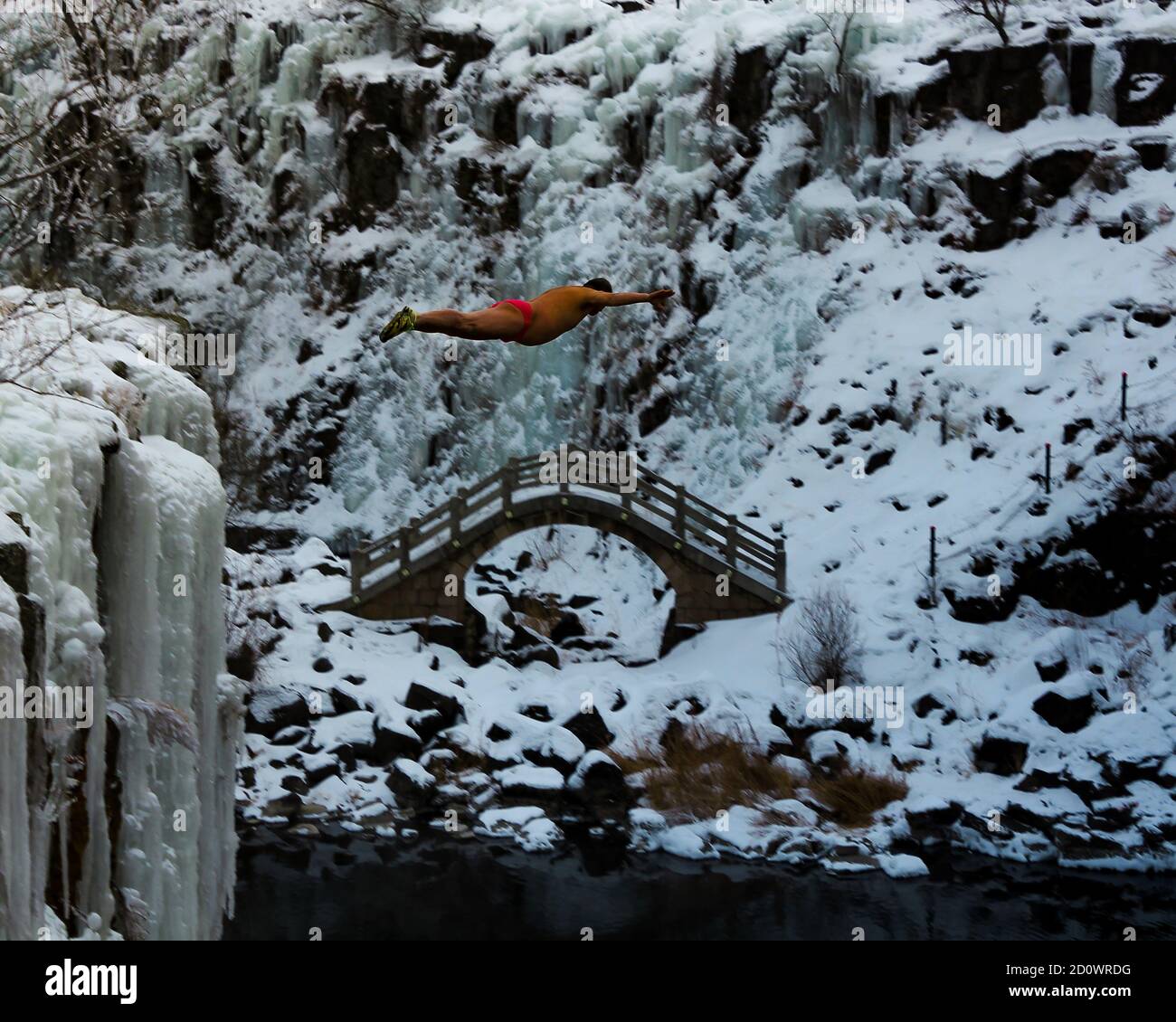 Un subacqueo salta da una scogliera in una piscina riscaldata vulcanicamente nel mezzo dell'inverno. Foto Stock