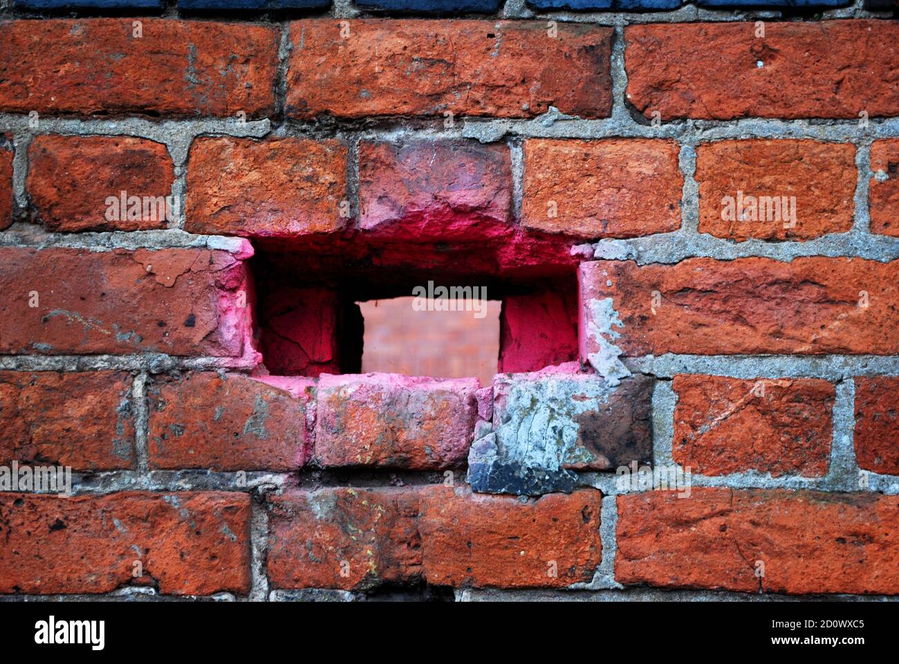 Un buco in un muro di mattoni che è stato spray verniciato rosa Foto Stock