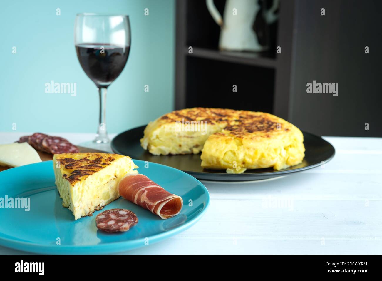 Frittata di patate con prosciutto e salsiccia su un piatto blu con un bicchiere di vino su sfondo bianco. Spazio di copia. Foto Stock