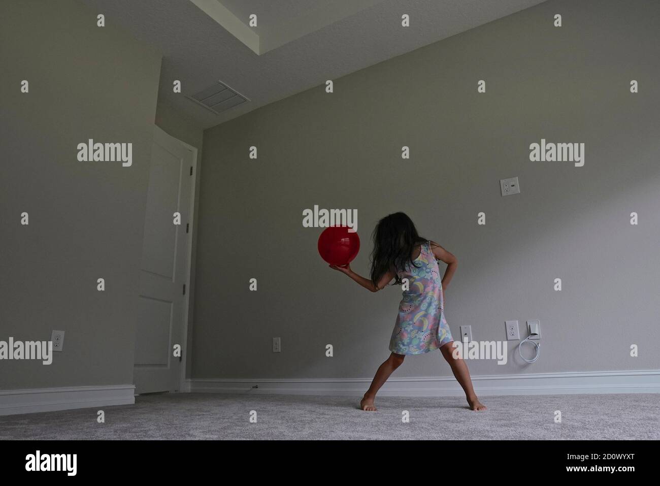 Ragazza di cinque anni che gioca con un palloncino rosso dentro una stanza vuota Foto Stock
